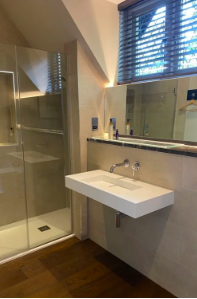 Modern bathroom with a glass-enclosed shower, a white rectangular sink, and a large mirror. There is a window with blinds above the sink.