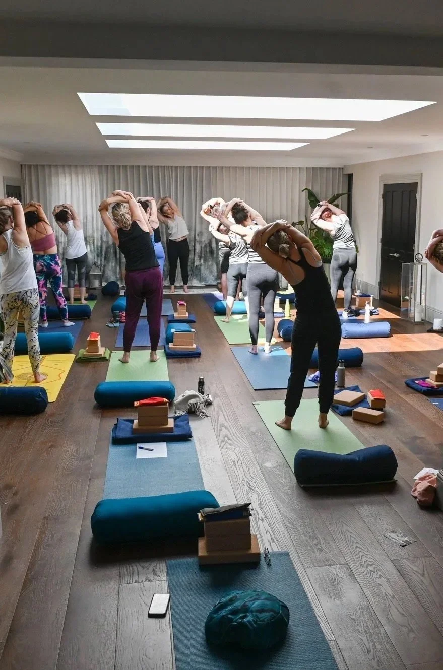 People participating in a yoga class in a well-lit studio with mats, blocks, and bolsters.