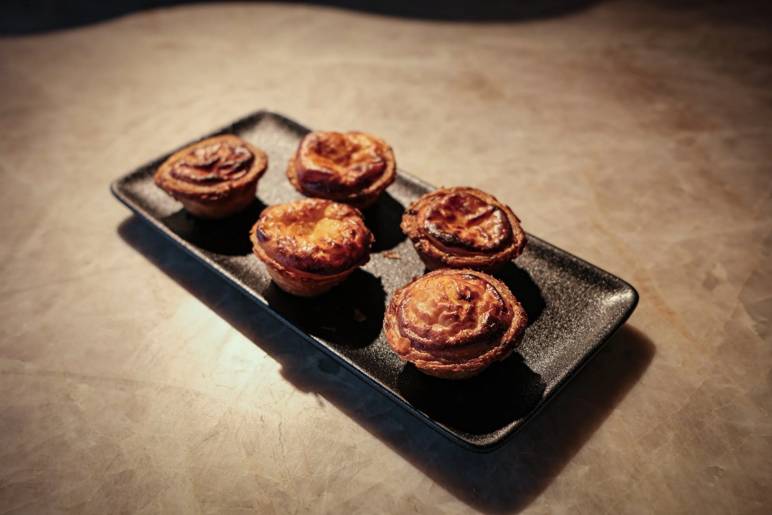 Vijf mini egg tarts op een zwart bord.