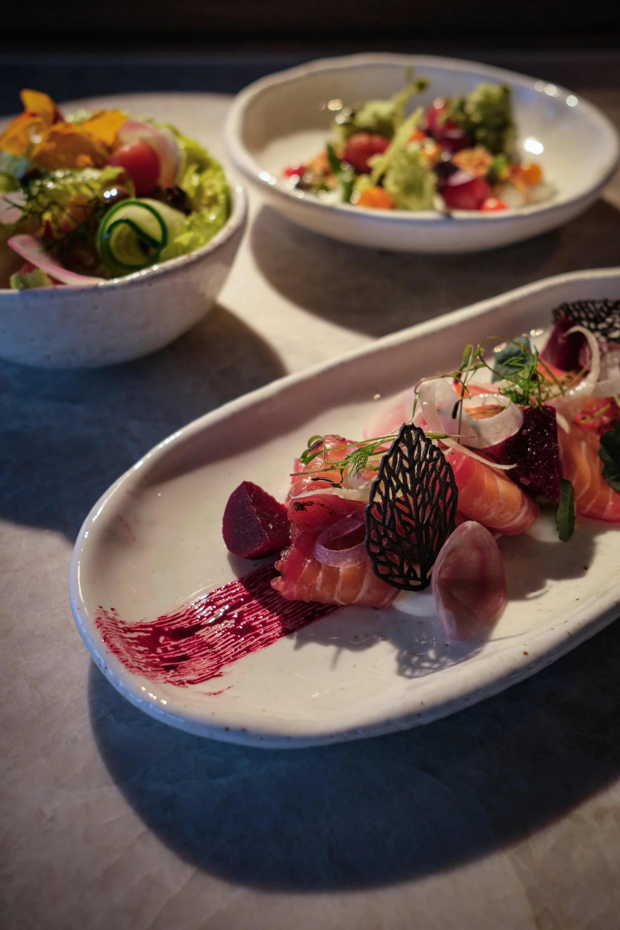 Gepresenteerde gerechten met rauwe vis, salade en verschillende garnituren, geserveerd op witte zilveren schalen en kommen.