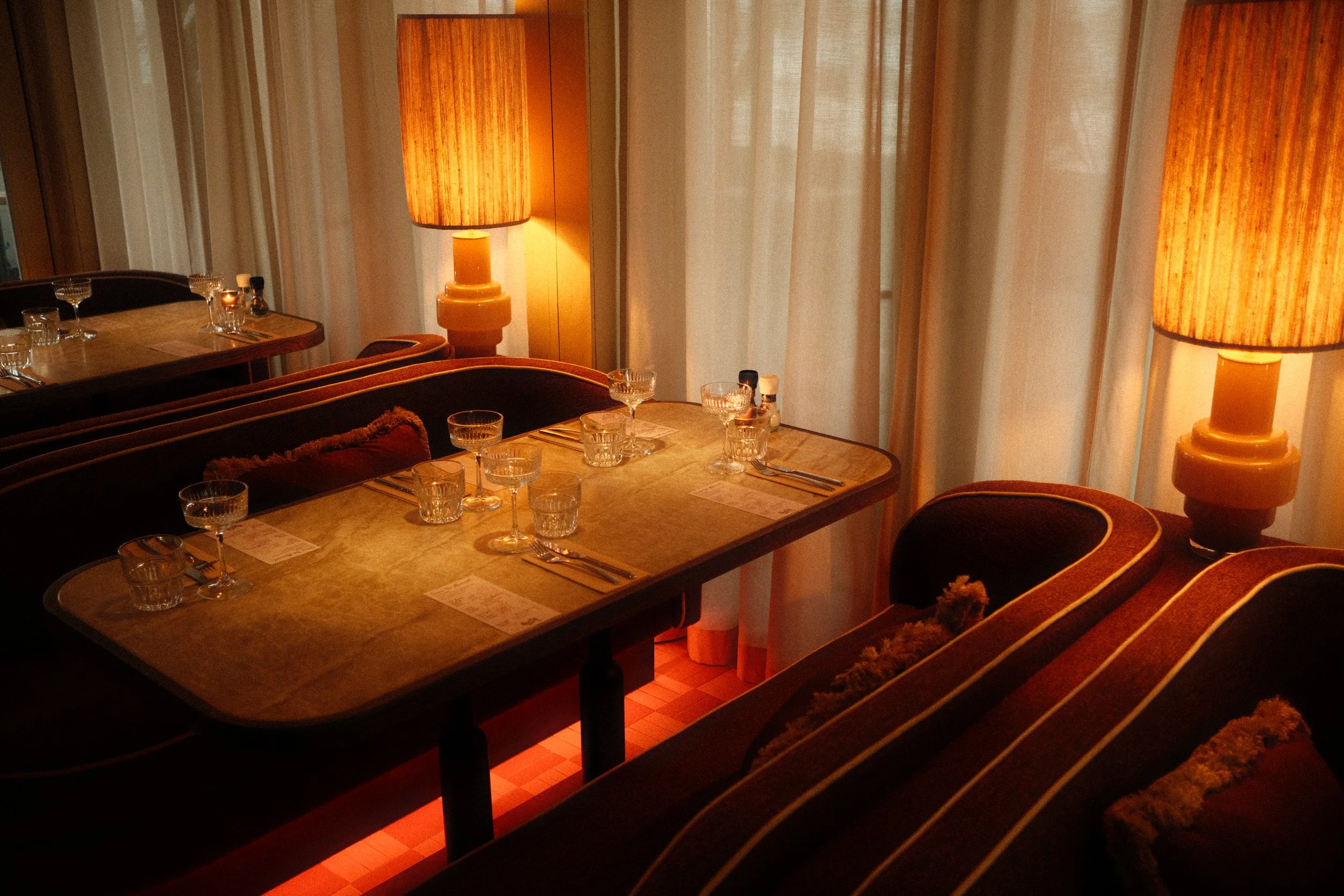 Een sfeervol restaurant met lage tafels, lampen en banken, klaar voor gasten met bestek en glazen, warme verlichting