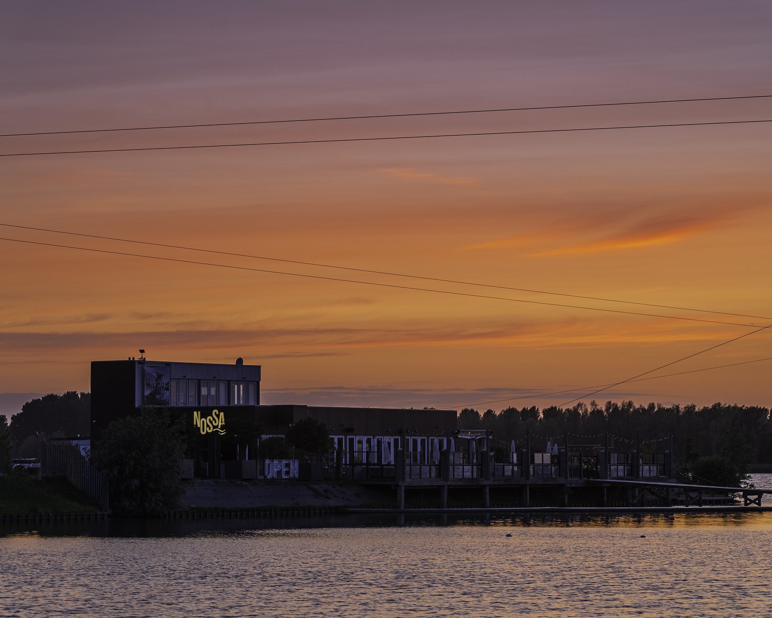 Een restaurant naast een rivier tijdens zonsondergang met een kleurrijke hemel.