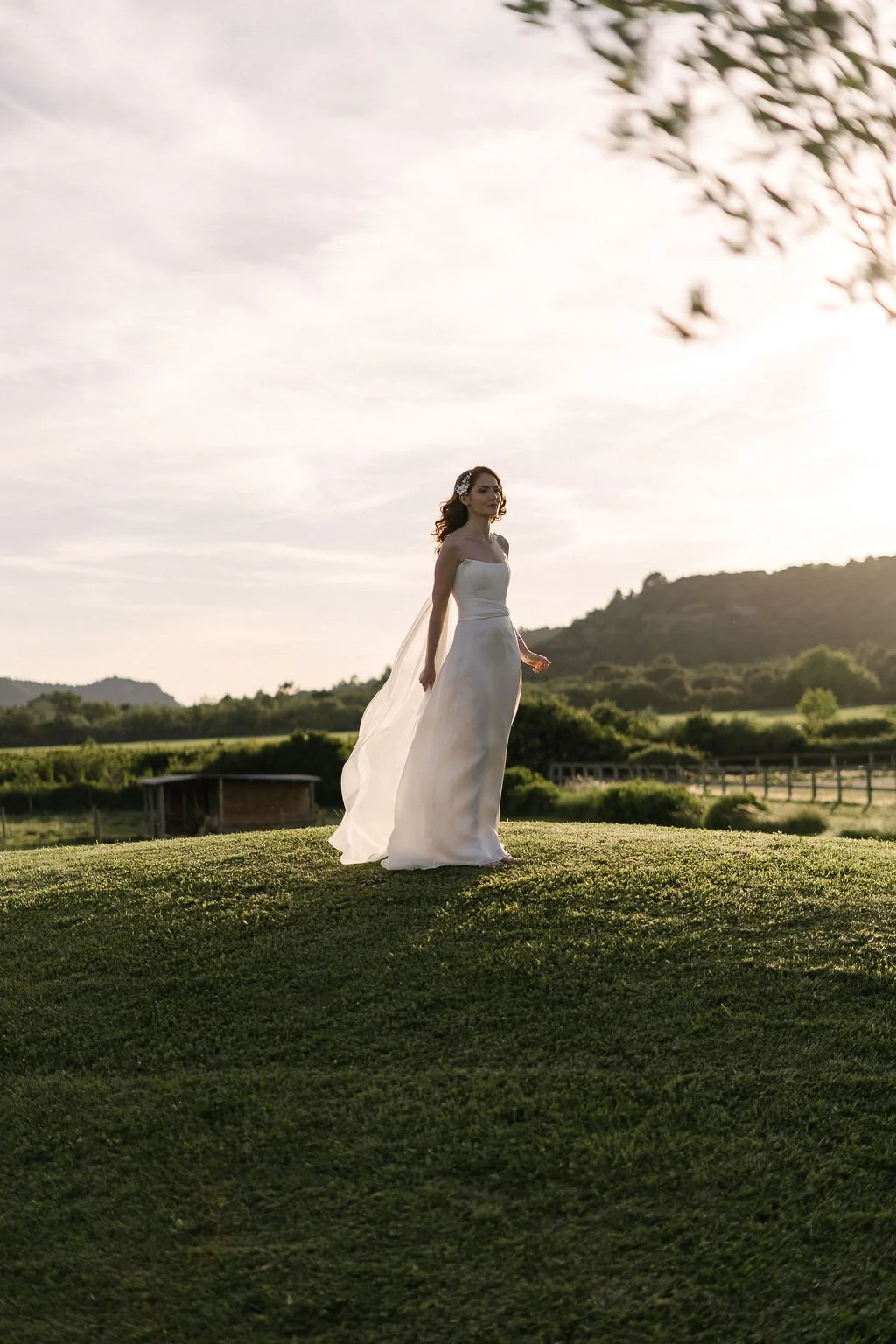 Photo d'une mariée sur une petite bute de pelouse au soleil couchant dans un domaine du Luberon, on la distingue en transparence de sa robe de mariée.