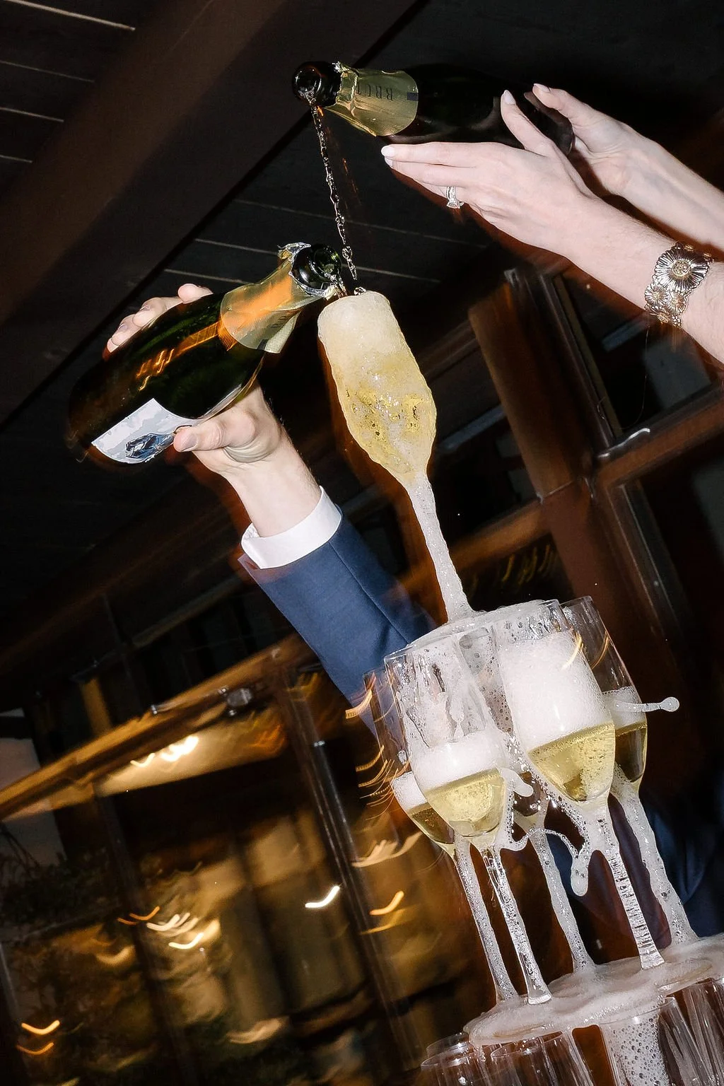 Deux personnes vident des bouteilles de champagne dans des coupes, créant un cascade de champagne dans des verres empilés. photo de soirée de mariage au flash.