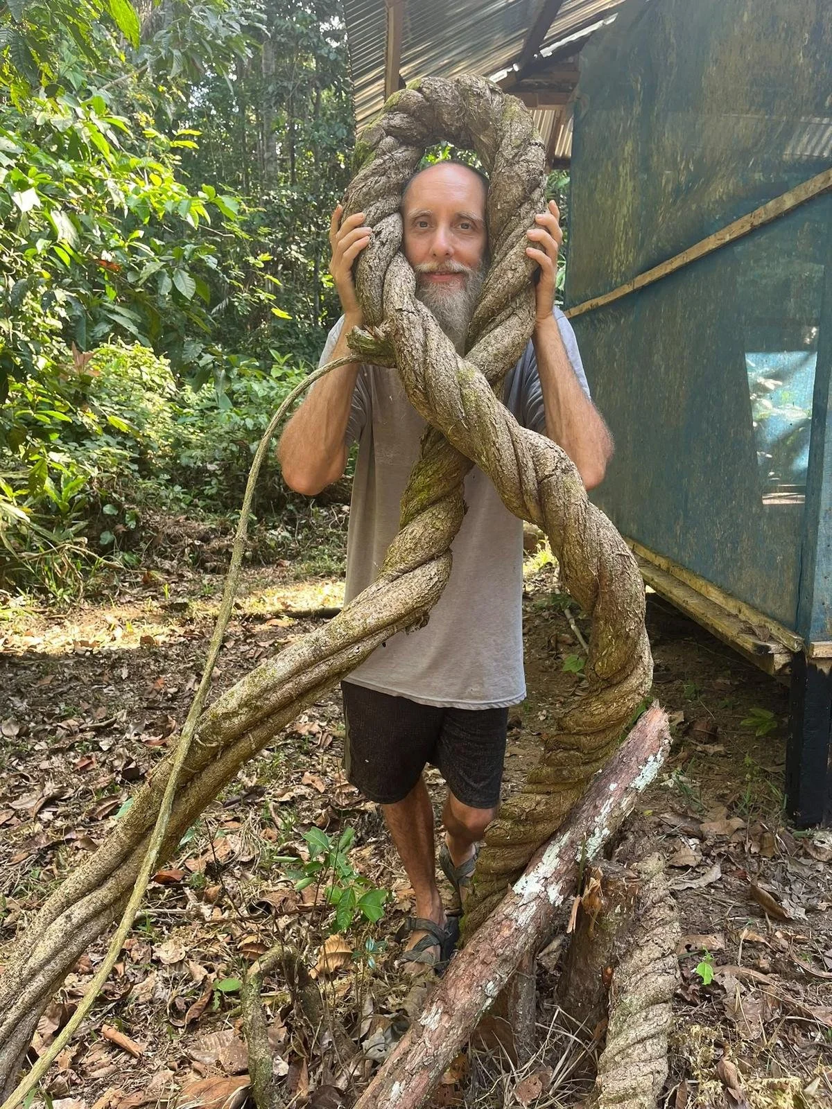 Greg Forret holding a giant twisted jungle vine in the Amazon rainforest at Rebirth Healing Center