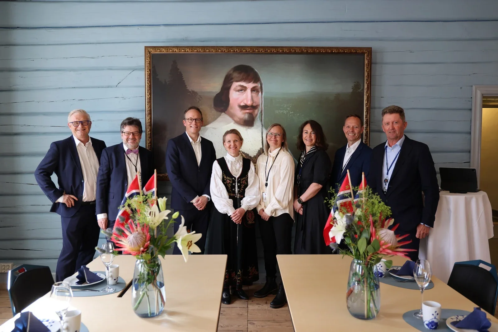 En gruppe mennesker i formell bekledning stående foran et portrettmaleri av kong Christian 4. i Auditoriesalen på Bergseminaret.