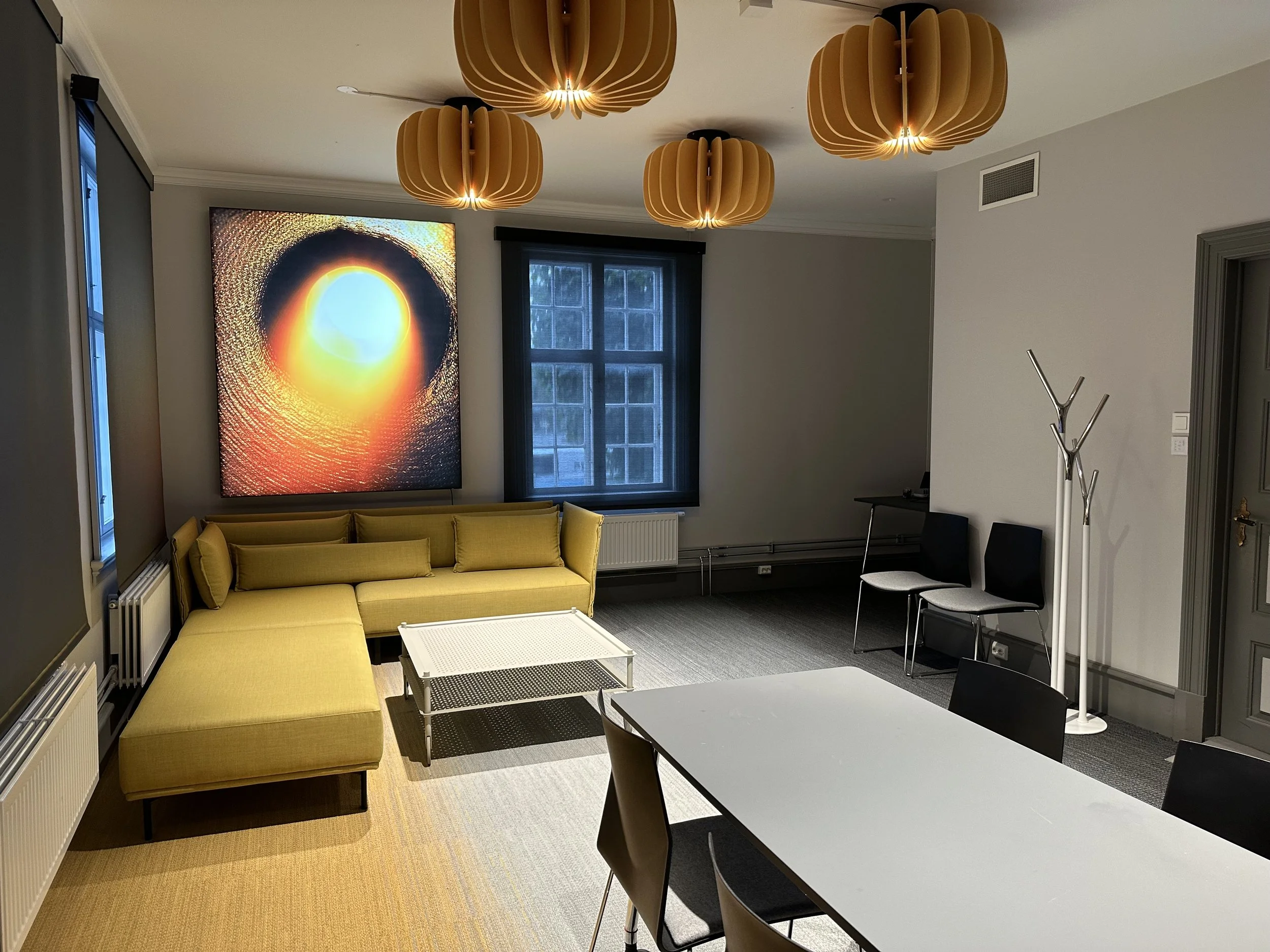 Et møterom med gul sofa, moderne gule taklamper, et bord og stoler.