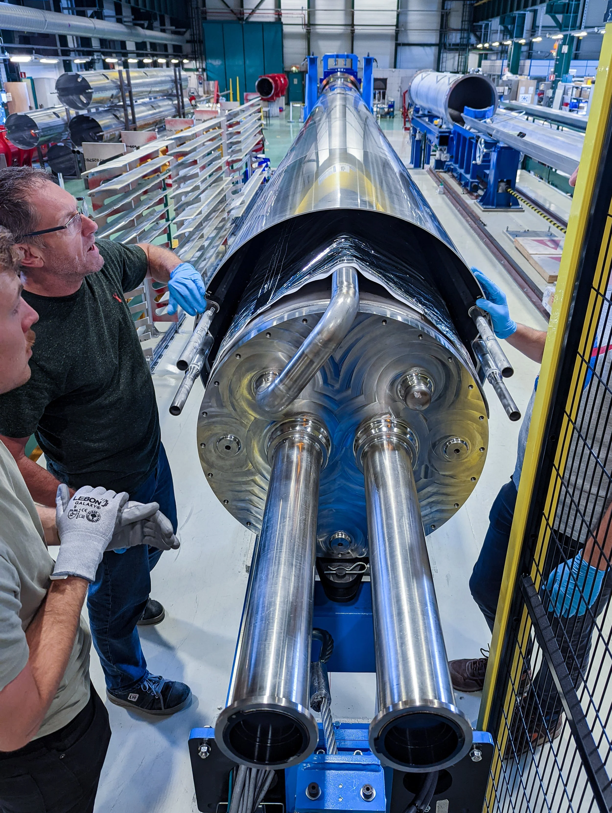 Three workers inspecting a large rocket engine inside a manufacturing facility.