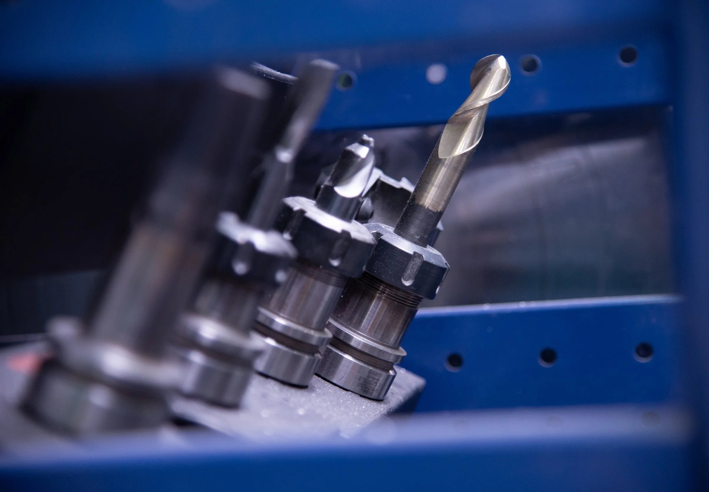 Close-up of precision drill bits stored in a blue metal rack, used for machining or manufacturing.