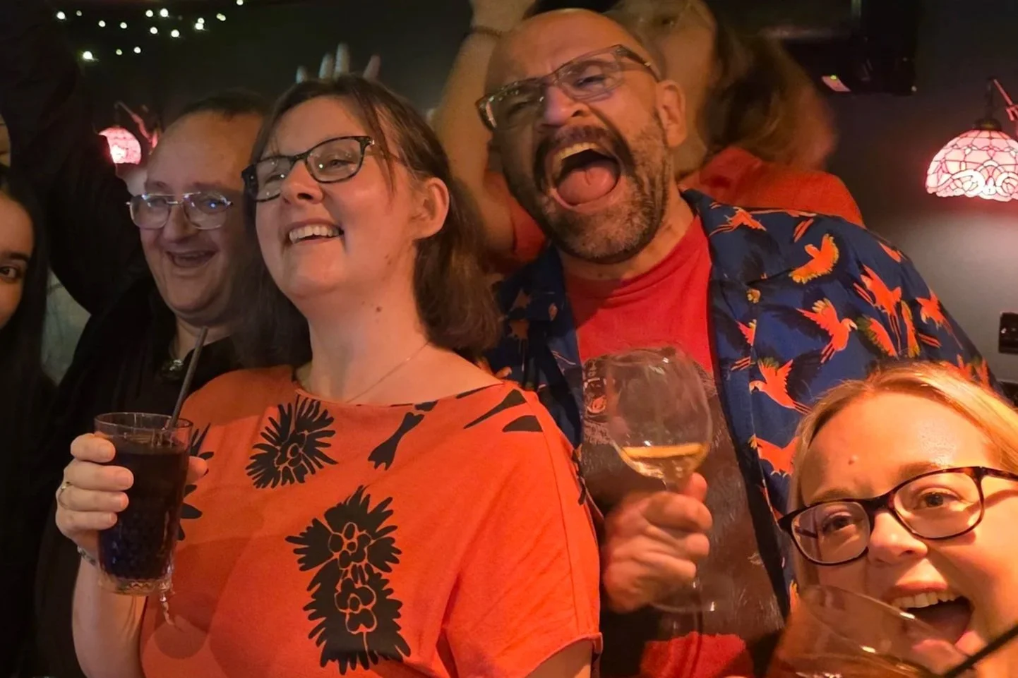 Group of people enjoying a night out, smiling, and holding drinks, with some wearing colorful tropical shirts.
