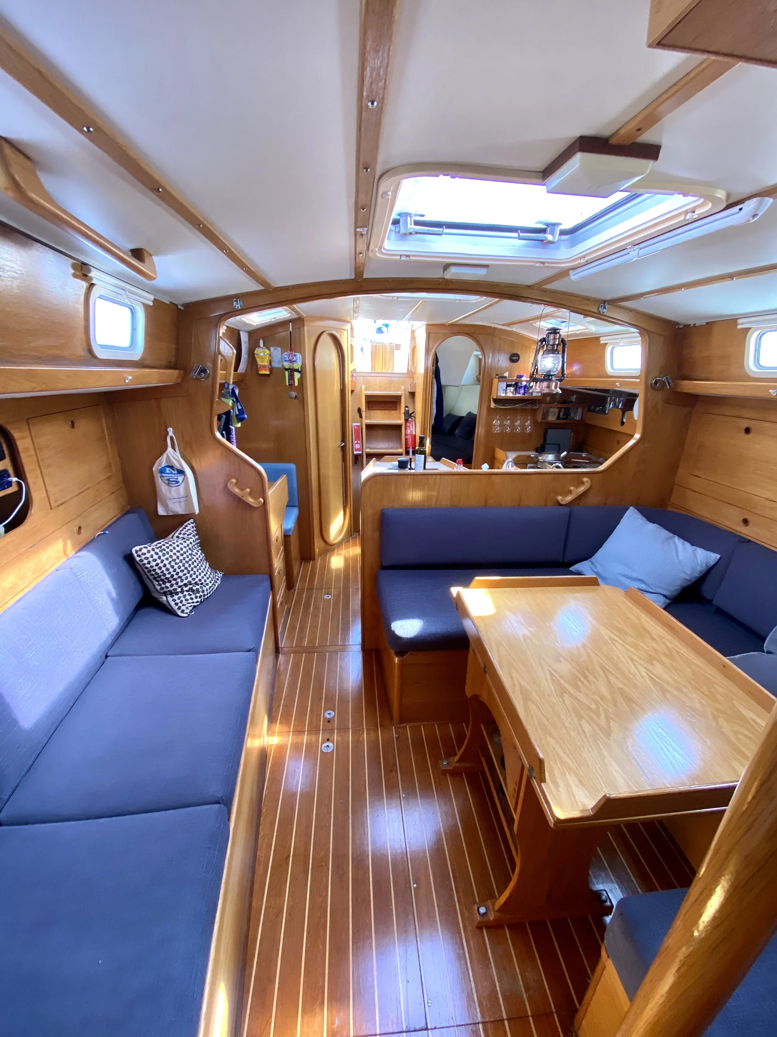 Interior of a wooden boat with blue cushioned seating, a wooden table, small windows, and a skylight.