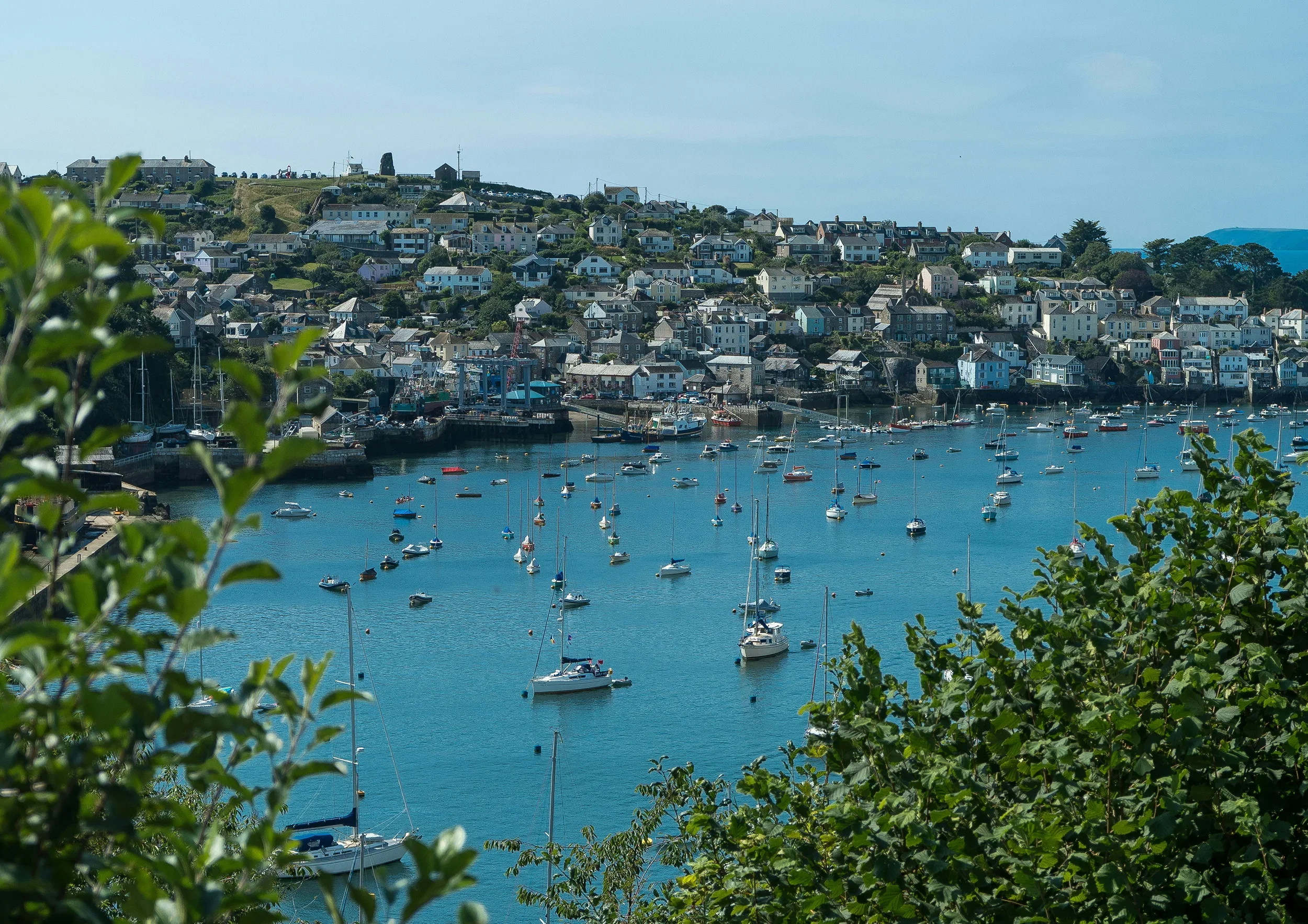 A sailboat on calm ocean waters heading towards a lighthouse in the distance under a partly cloudy sky.