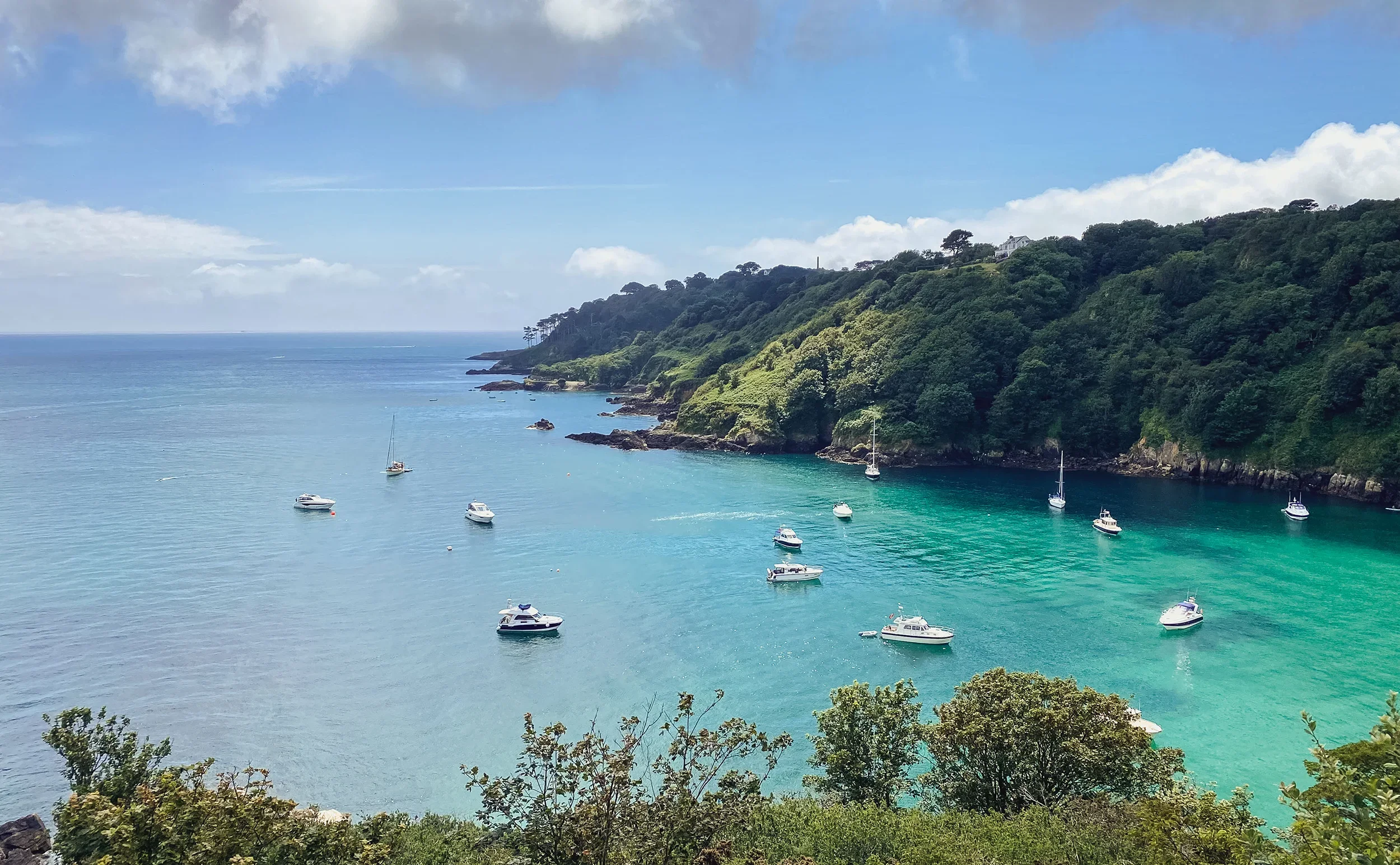 A sailboat on calm ocean waters near rocky shoreline with a clear sky in the background.