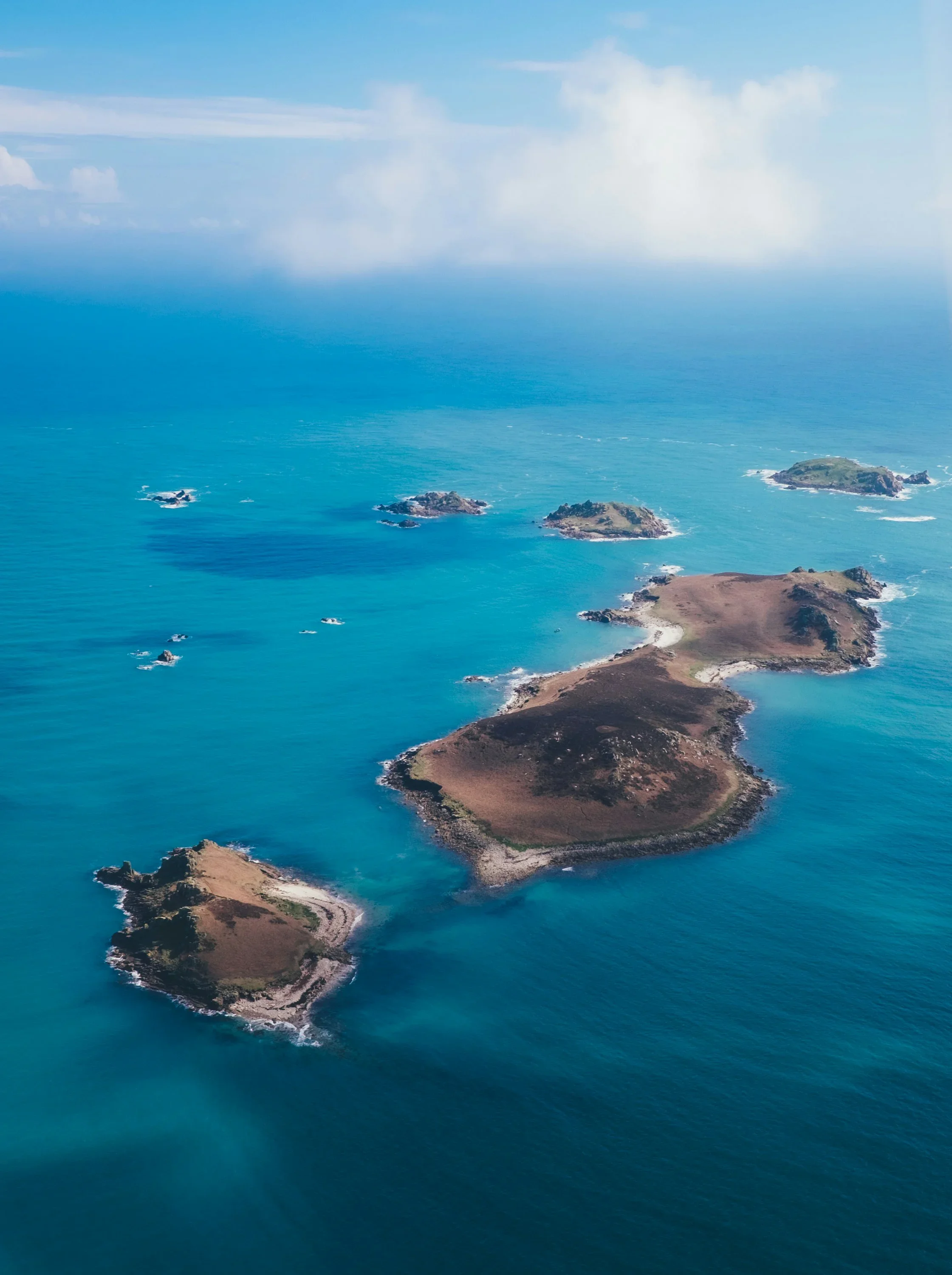 Aerial view of a group of small islands surrounded by blue ocean water, with some patches of grassy terrain and rocky coastlines.
