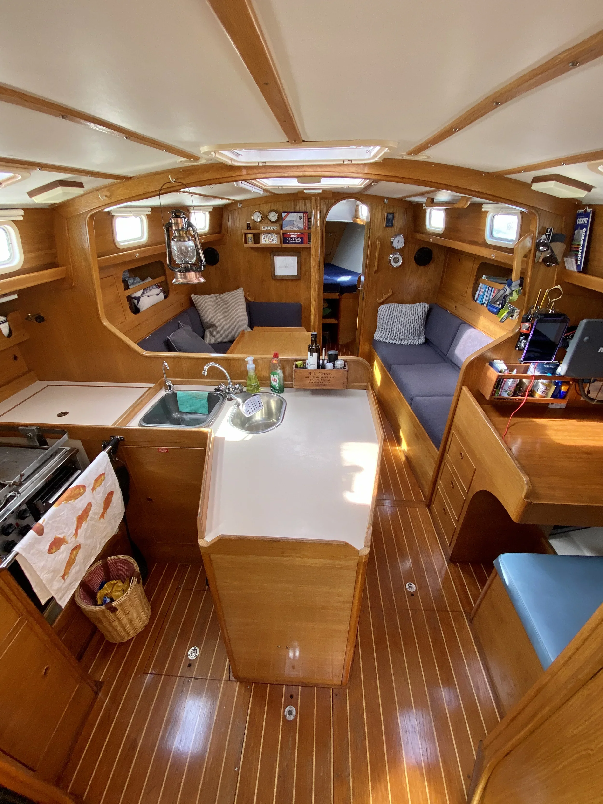 Interior of a boat with wooden paneling, a small kitchen area with a sink, counter, and a stove, seating areas with cushions, and various decorations and equipment.