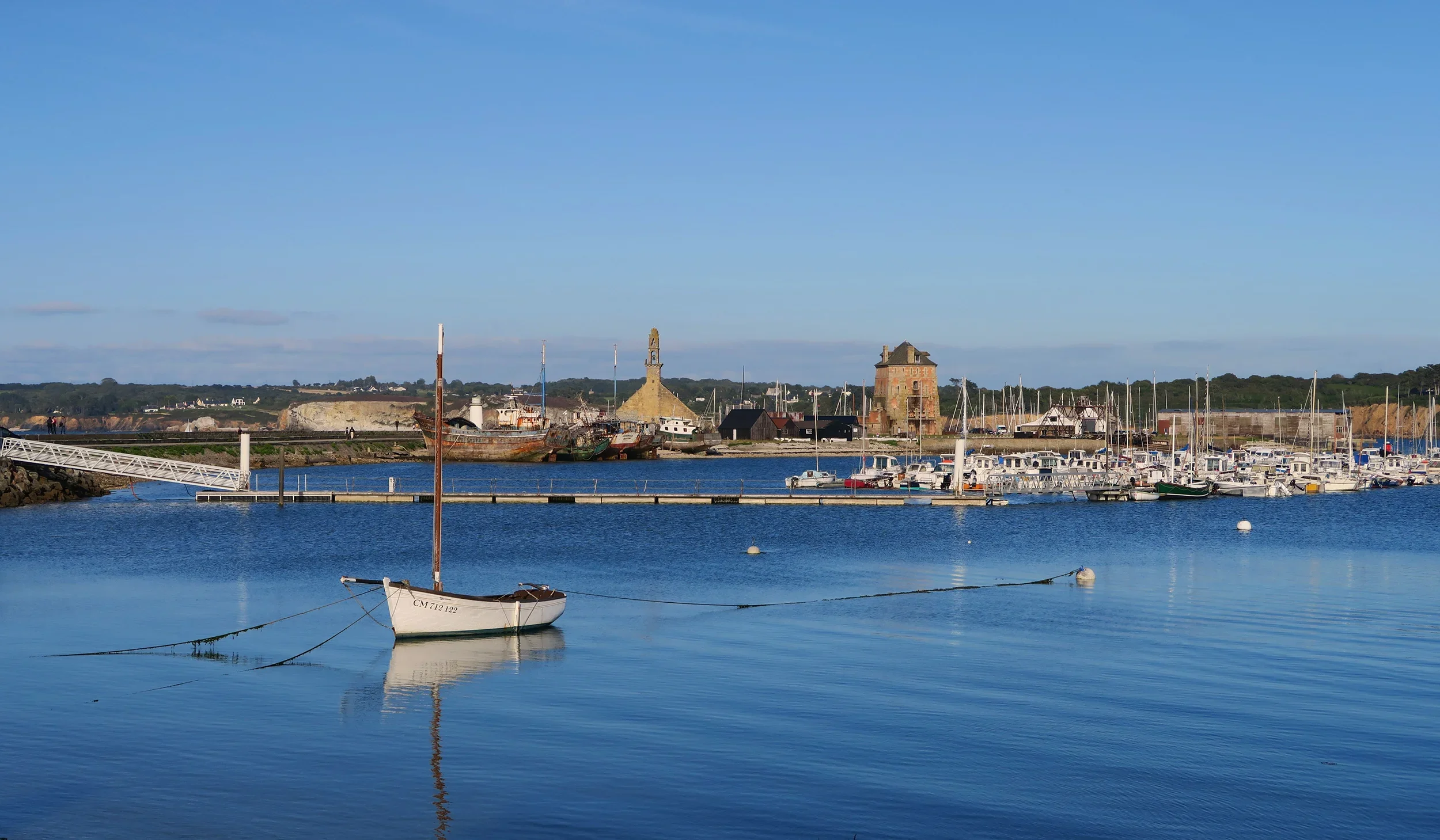 A harbor with boats docked and a lighthouse in the background on a clear day.