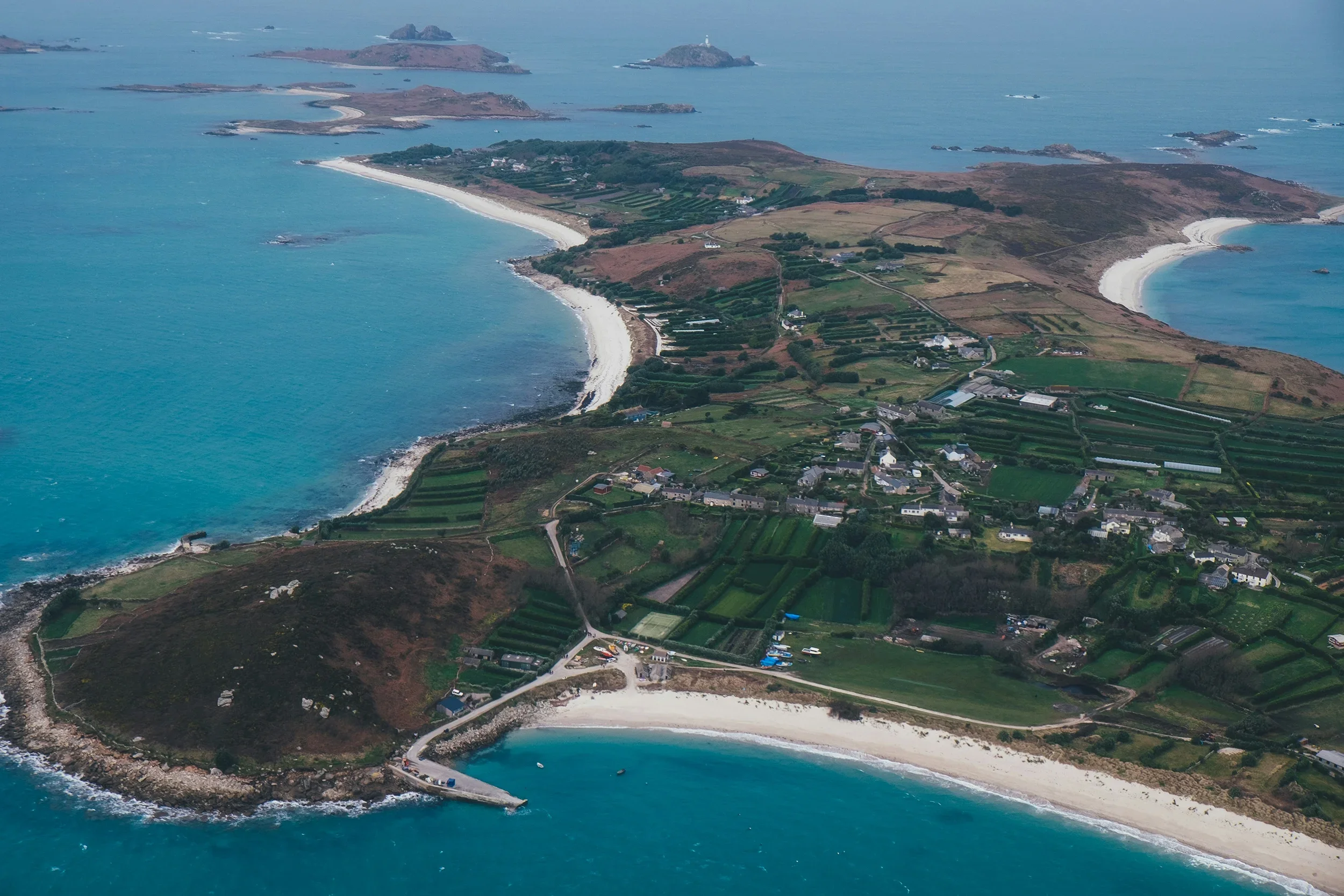 Aerial view of a coastal landscape featuring sandy beaches, green fields, scattered houses, and small islands across the ocean.