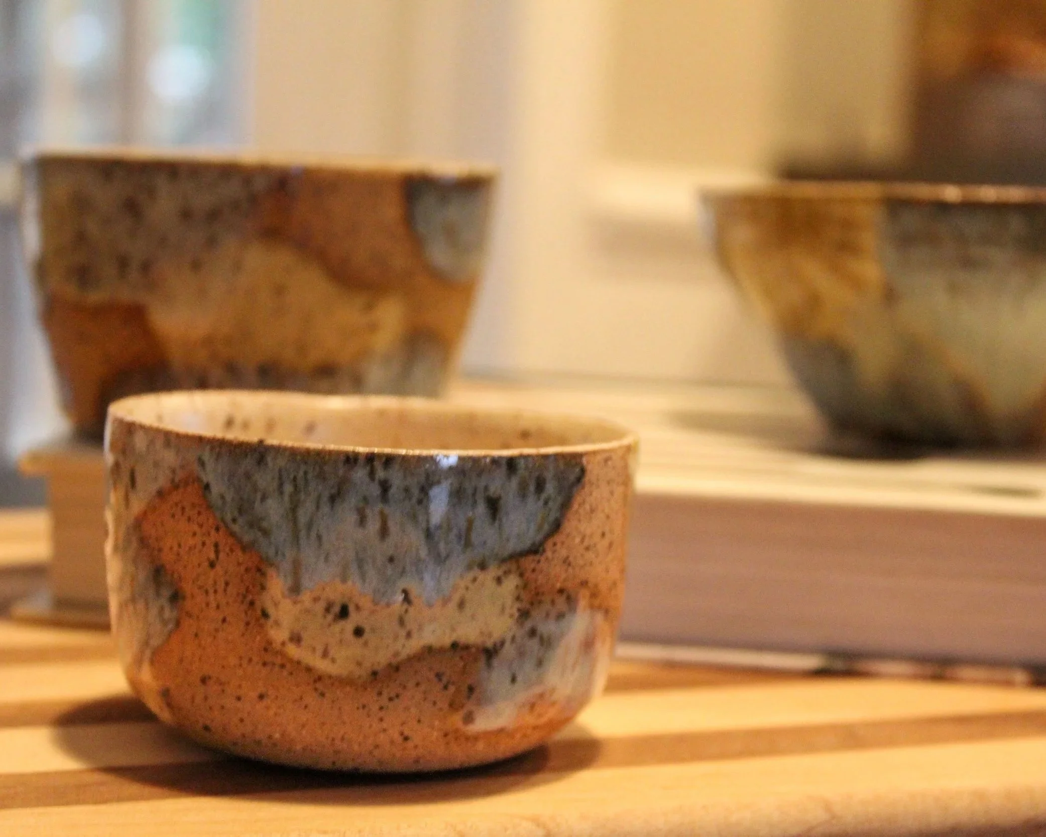 Close-up of three rustic ceramic bowls with a textured, multicolored finish, placed on a wooden surface with a blurred background.