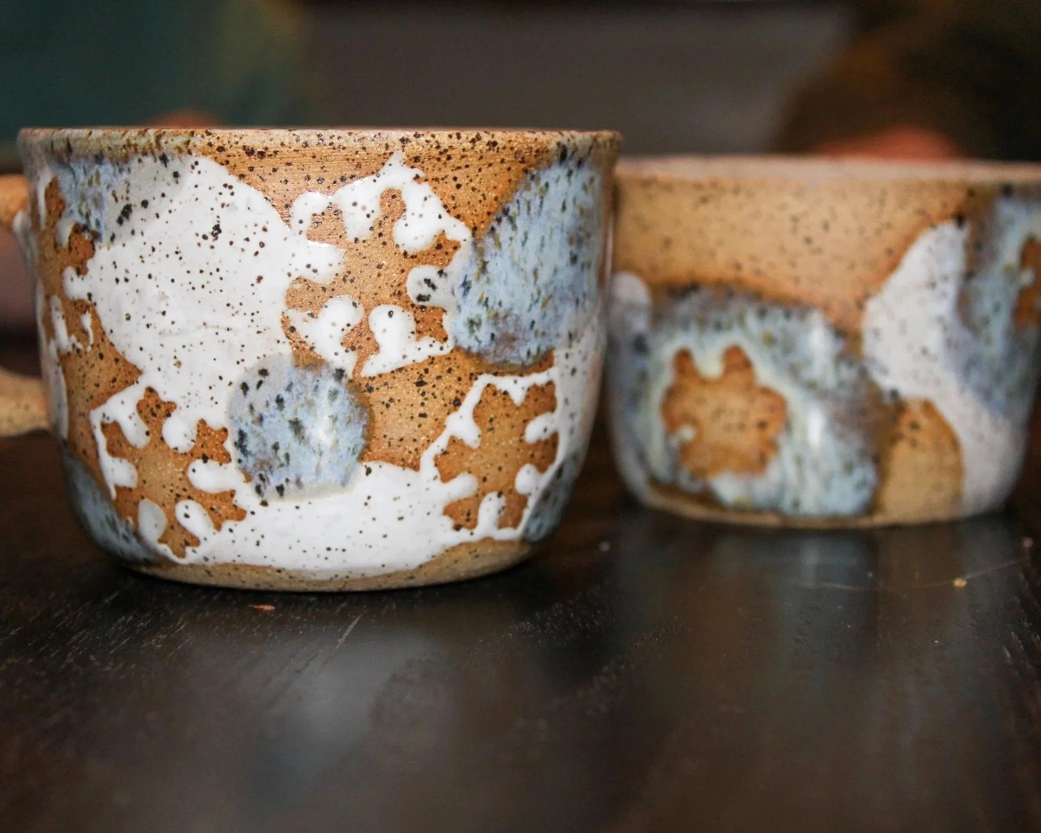 Close-up of two ceramic cups with abstract glaze patterns on a dark surface.