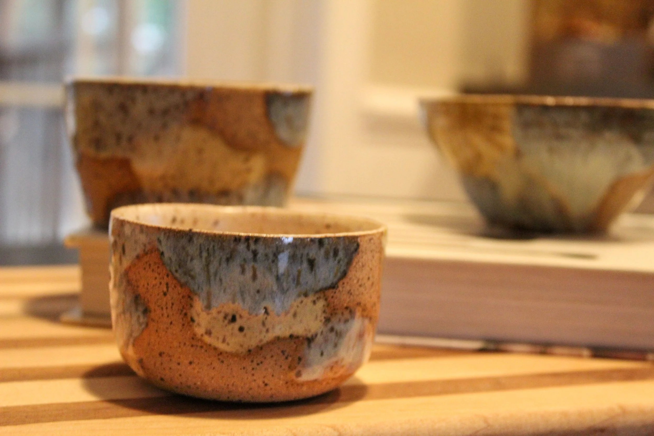 Three ceramic bowls with multicolored, abstract patterns placed on a wooden surface with a book in the background.
