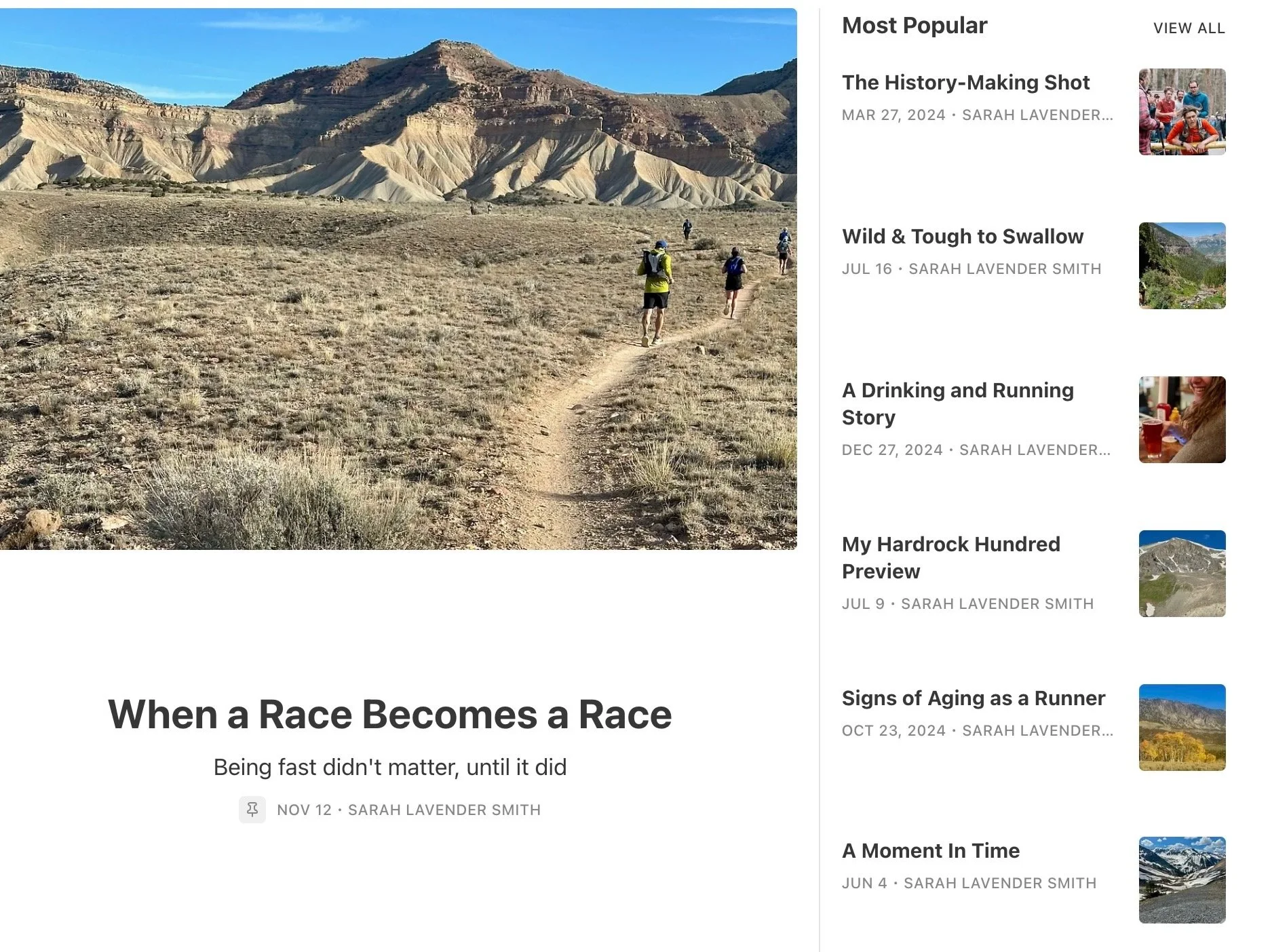 Hikers walking along a desert trail towards rugged, colorful mountains under a blue sky.