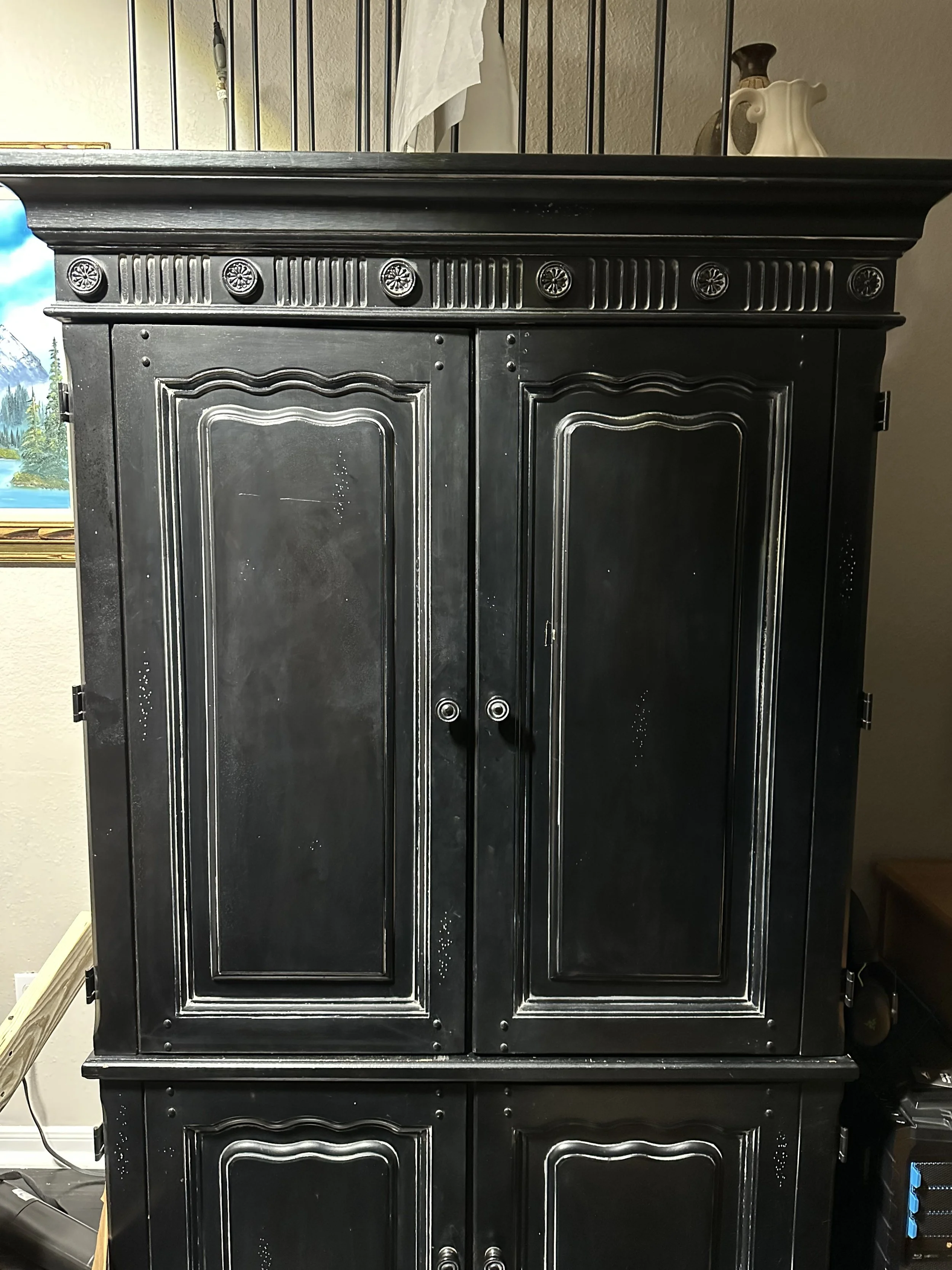 Large distressed black armoire with decorative rosette molding used for art supply storage in Timothy Chappell's painting studio. The cabinet is closed, concealing oil painting materials.