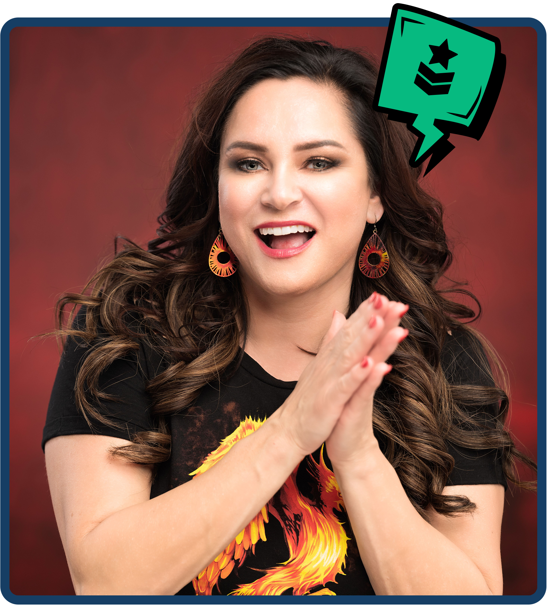A woman with long, wavy brown hair, wearing a black t-shirt with a fiery phoenix design, colorful earrings, and lipstick, smiling with her hands clasped in front of her, against a red background with a graphic of a speech bubble with military rank insignia.
