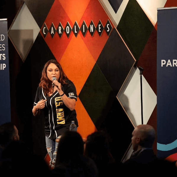 Woman speaking into a microphone on stage at Carolina's event with audience members watching.