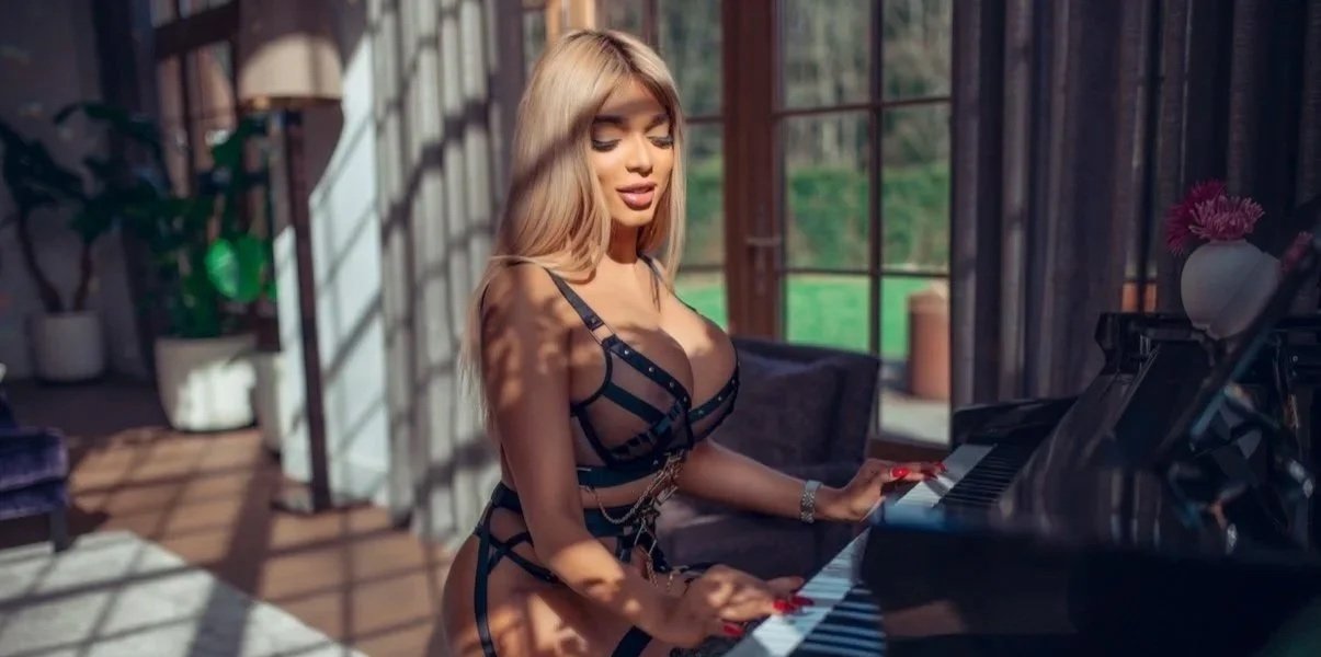 A woman with long blonde hair wearing black lingerie playing the piano in a sunlit room.