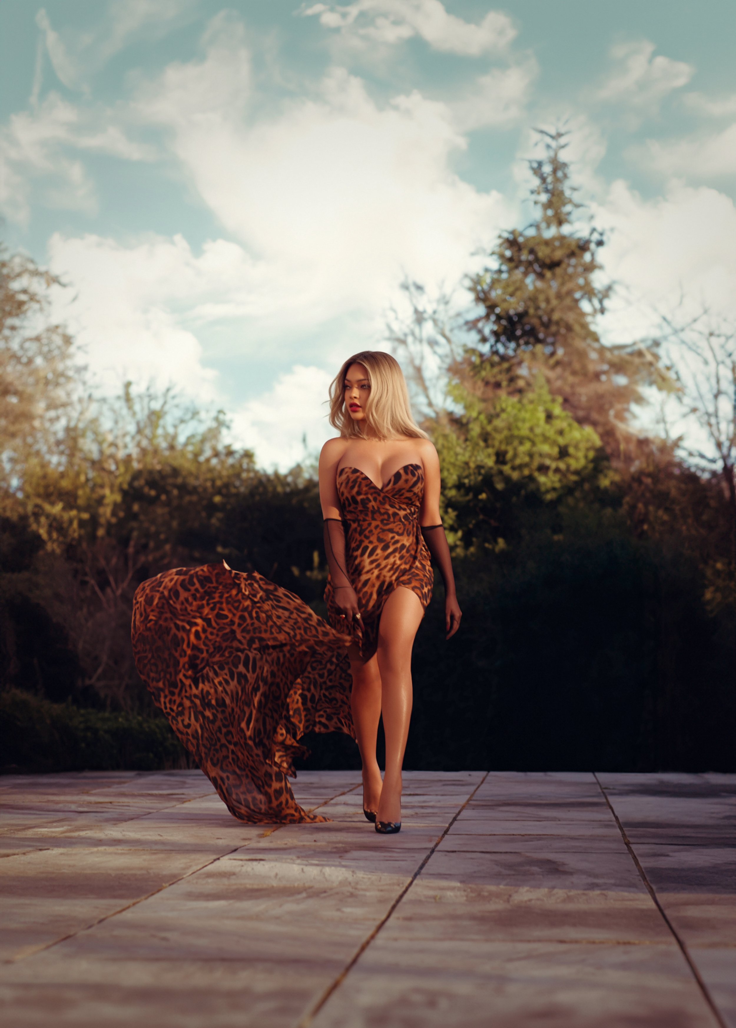 A woman in a leopard print dress with a thigh-high slit is walking on a tiled surface outdoors. The background has trees and a partly cloudy sky, and the woman is wearing high heels and black sheer gloves.