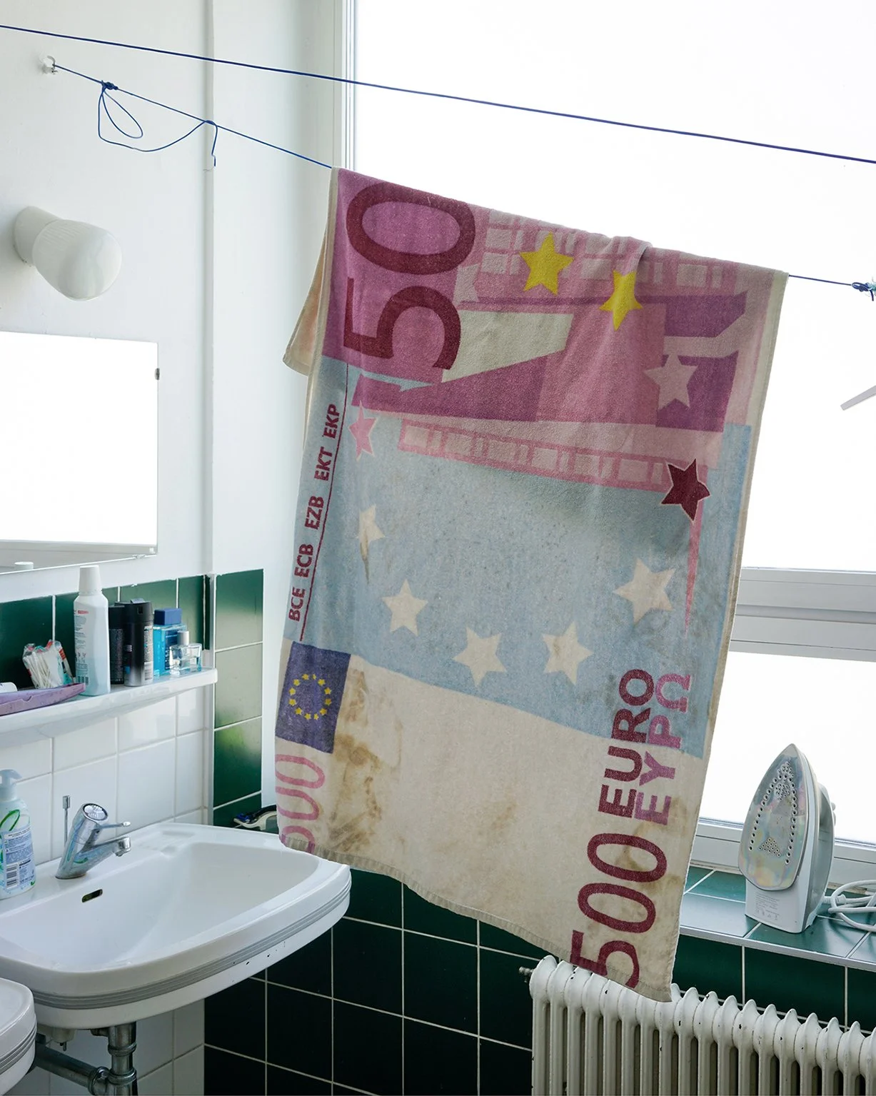A towel hanging on a clothesline inside a bathroom, with a design resembling a 50 euro banknote.