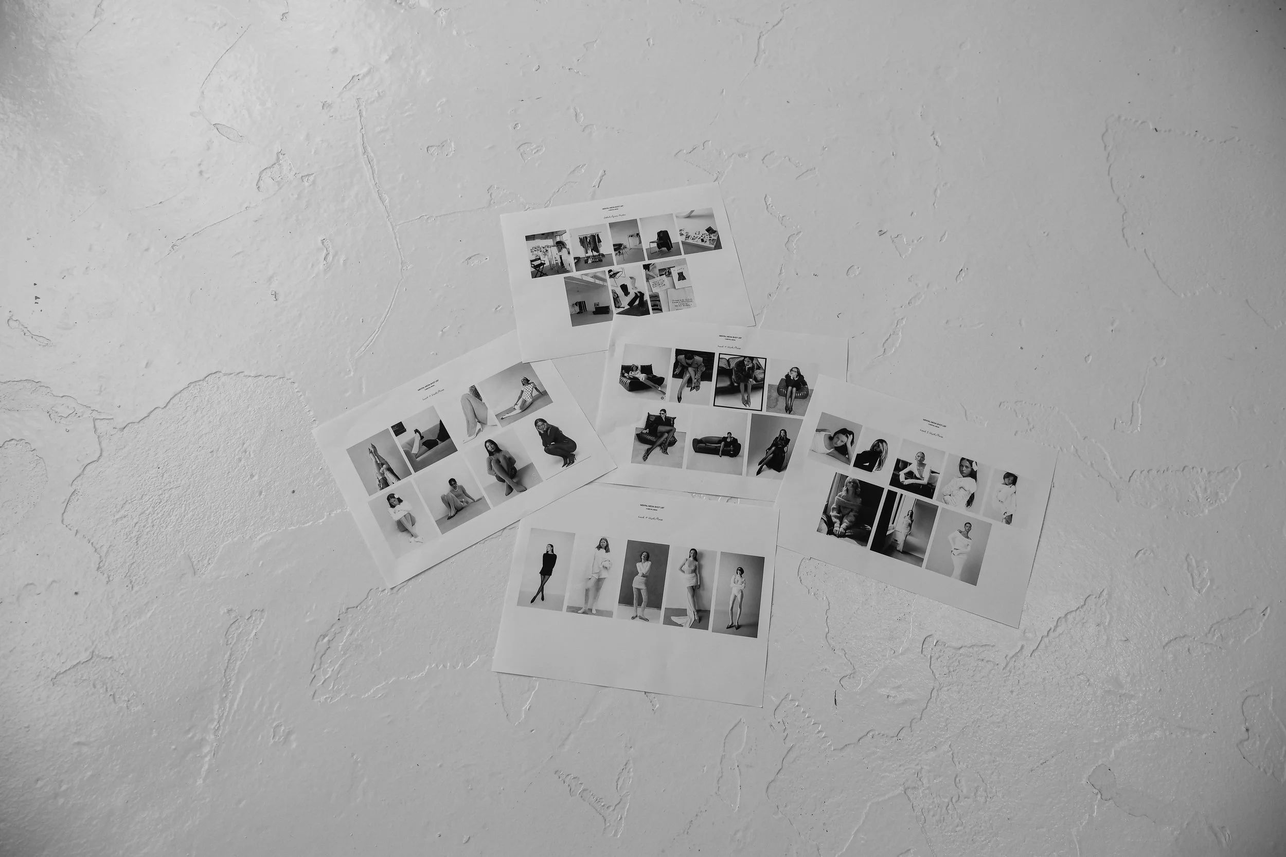 Four printed sheets of paper with black-and-white photographs of various models in different poses, spread out on a textured white wall.
