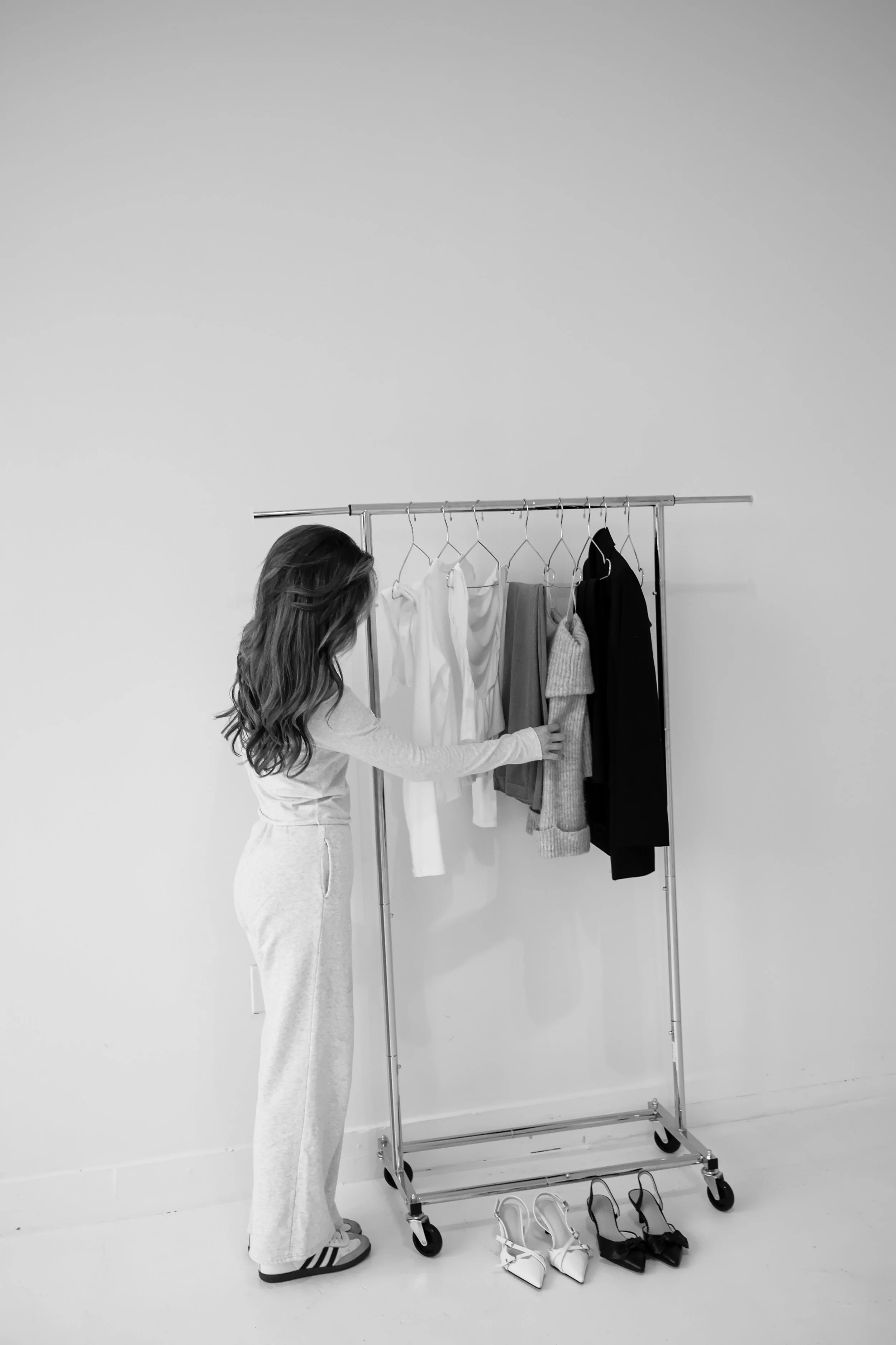 A woman in casual attire shopping for clothes from a mobile clothing rack with various garments and shoes.