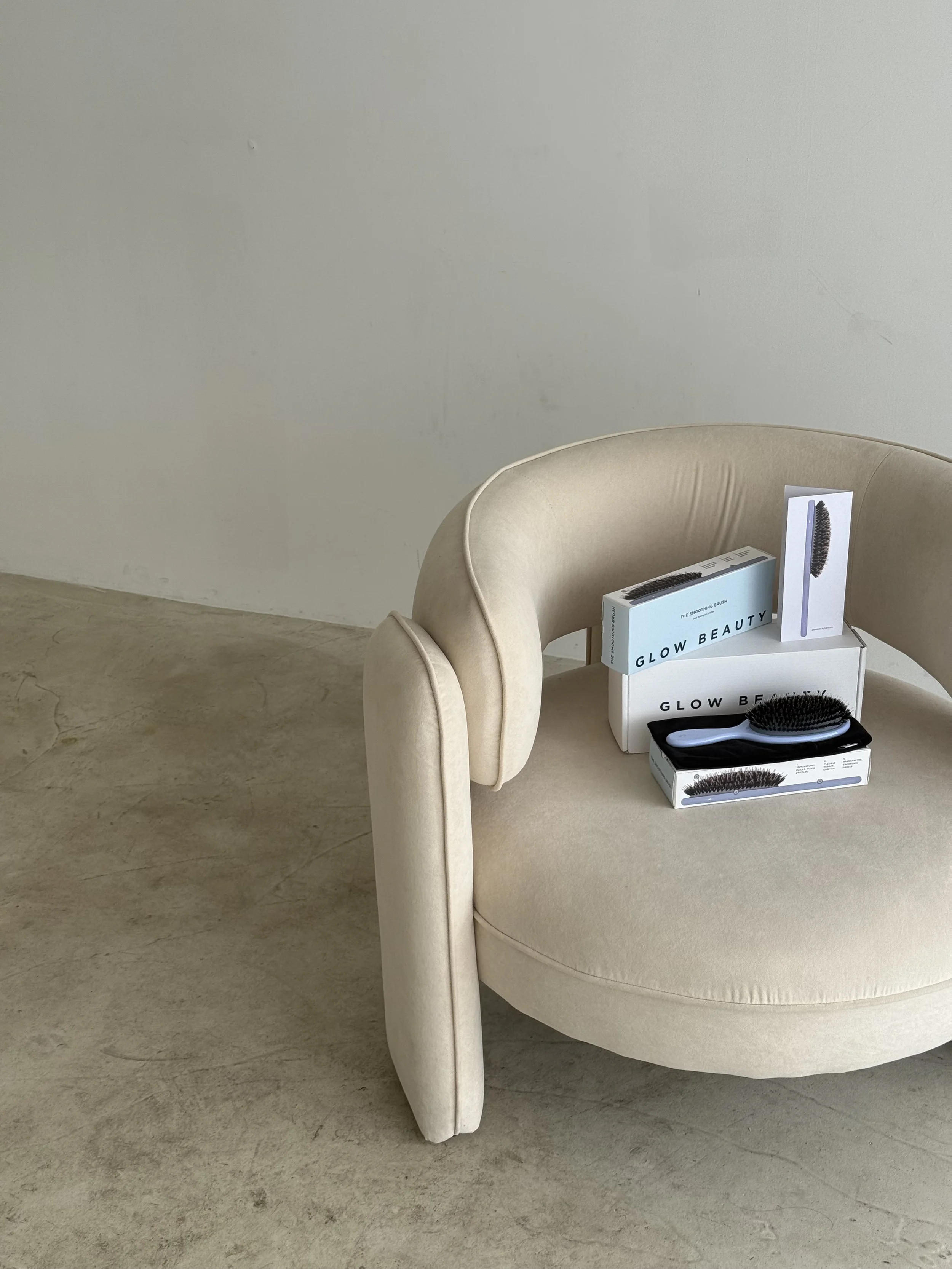 Beauty brushes and tools displayed on a beige cushioned chair with boxes labeled 'Glow Beauty' and 'Glow Beauty Brush'.