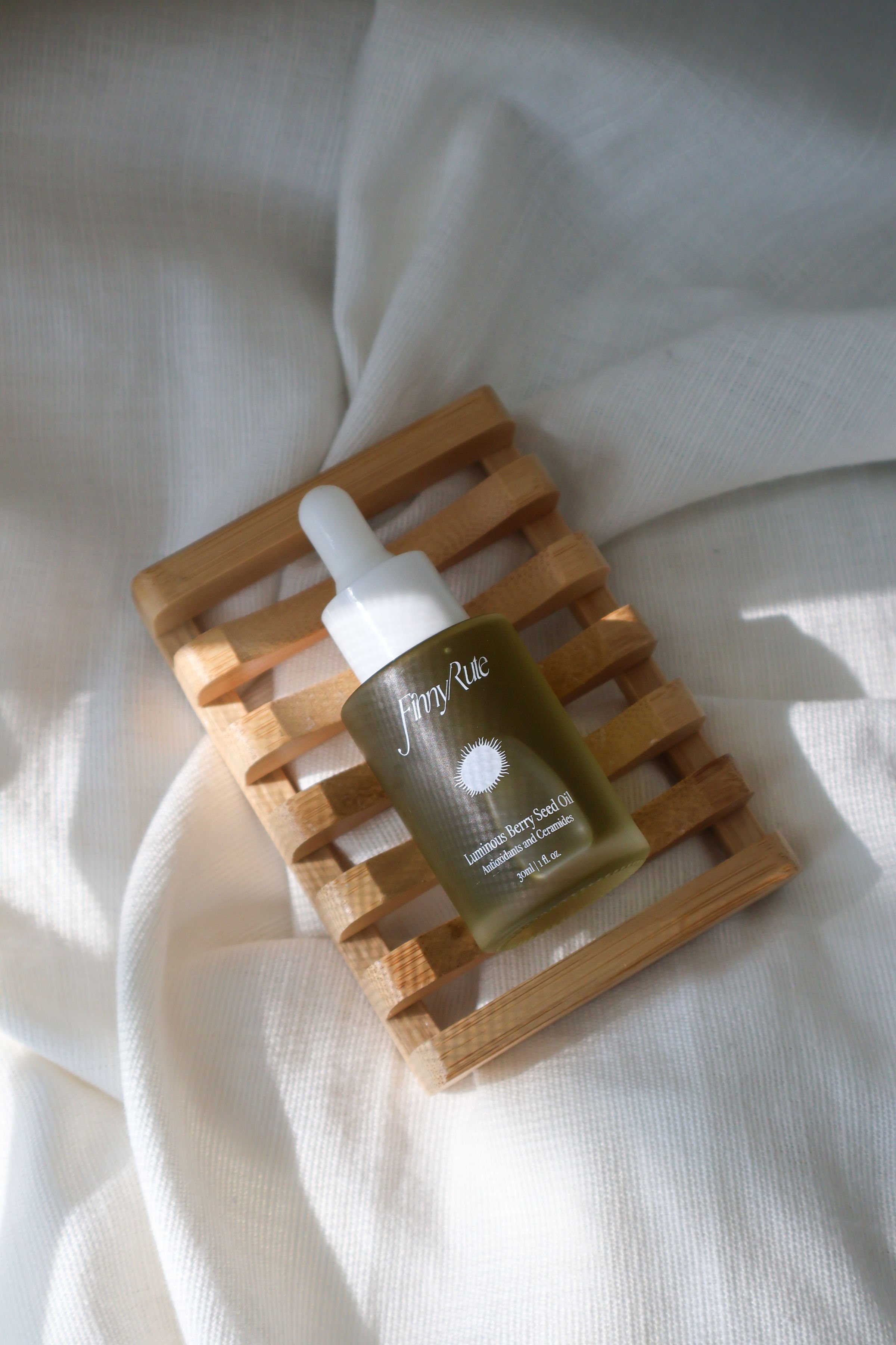 A bottle of FinnyRute luminous berry seed oil with a dropper cap, resting on a small wooden slatted tray on a white fabric background.