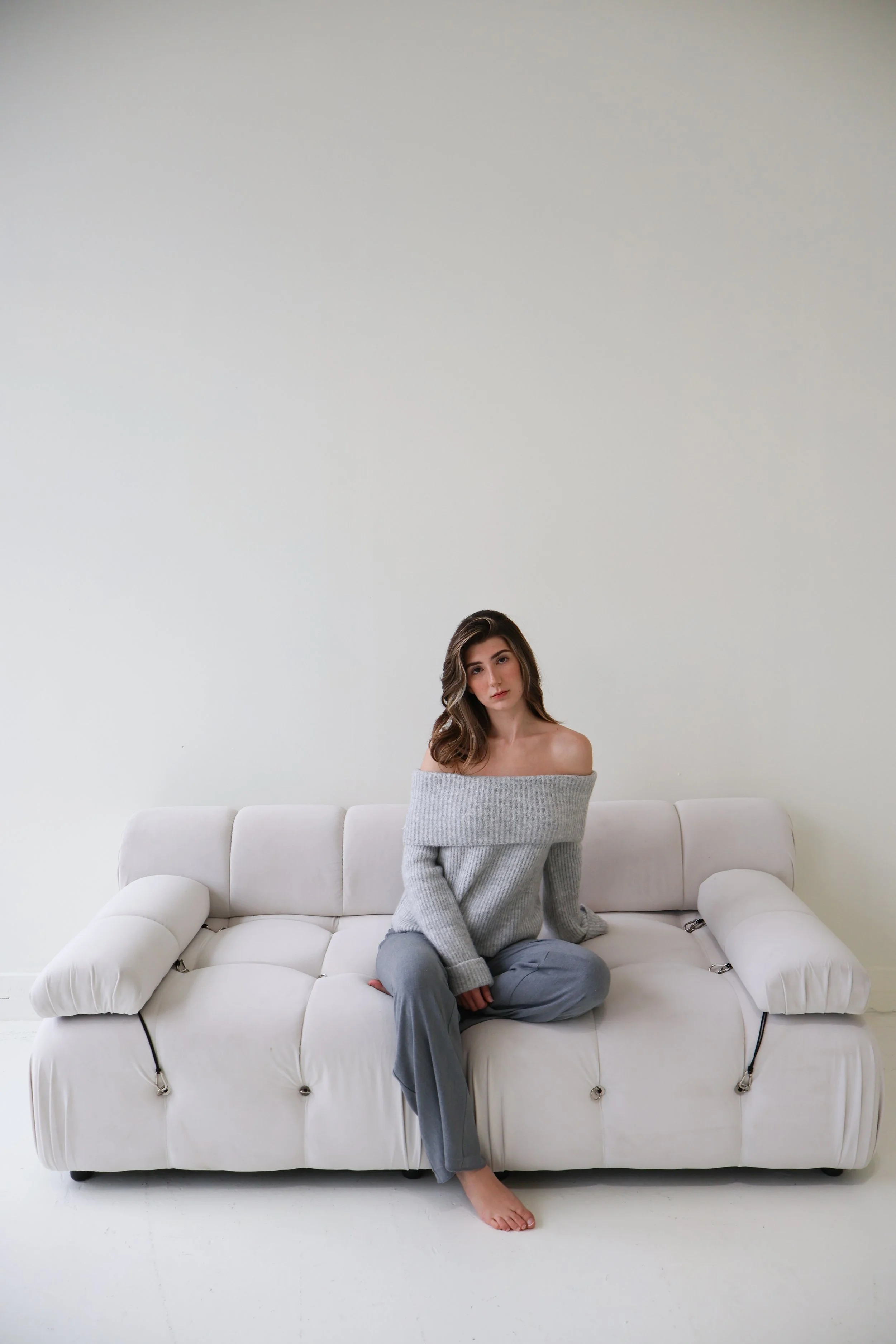 Young woman sitting on a white sofa in a minimalist room with blank white walls.