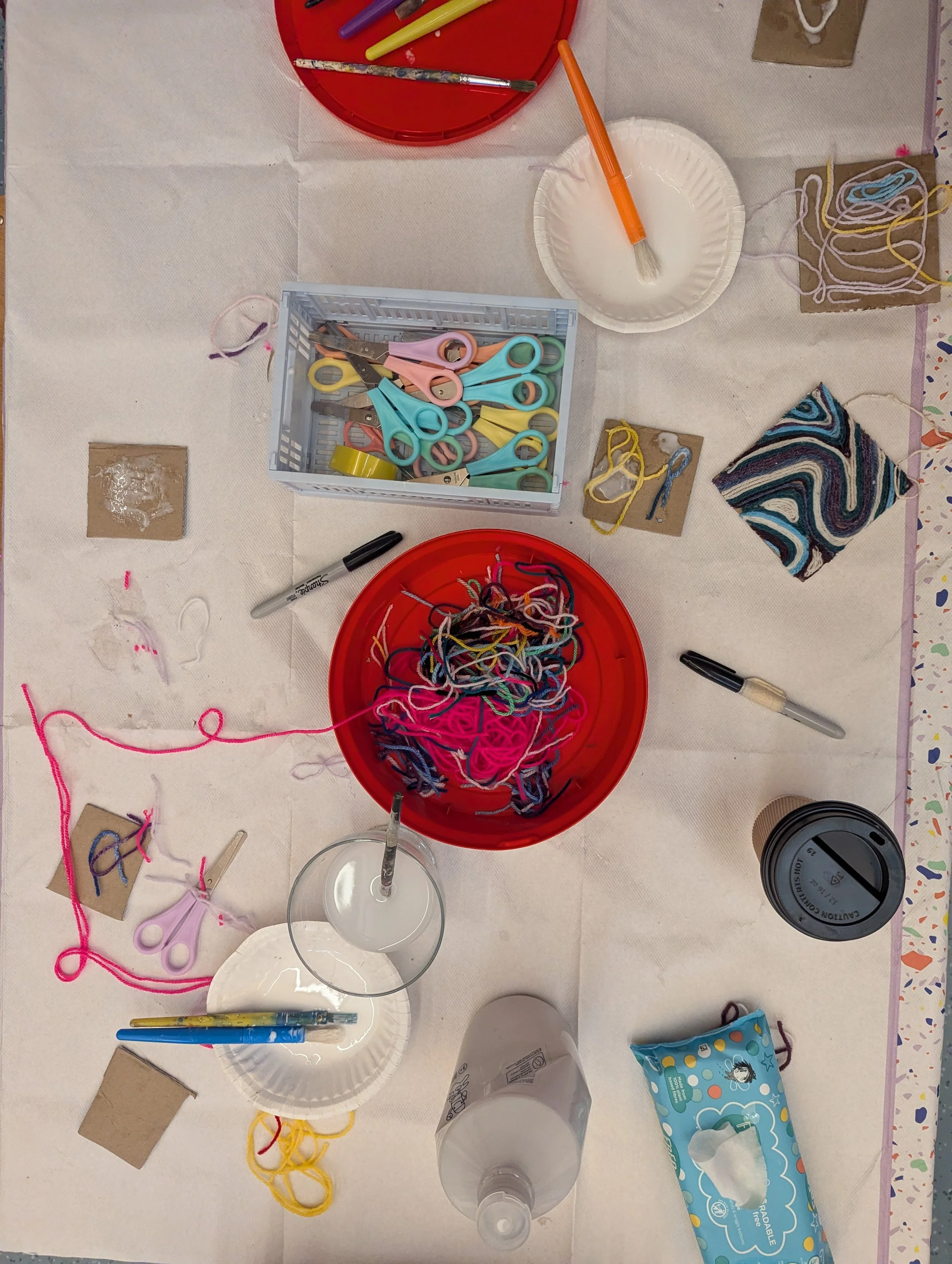 A craft table with colorful yarn, scissors, markers, a tissue box, and cups, organized for knitting or crocheting activity.
