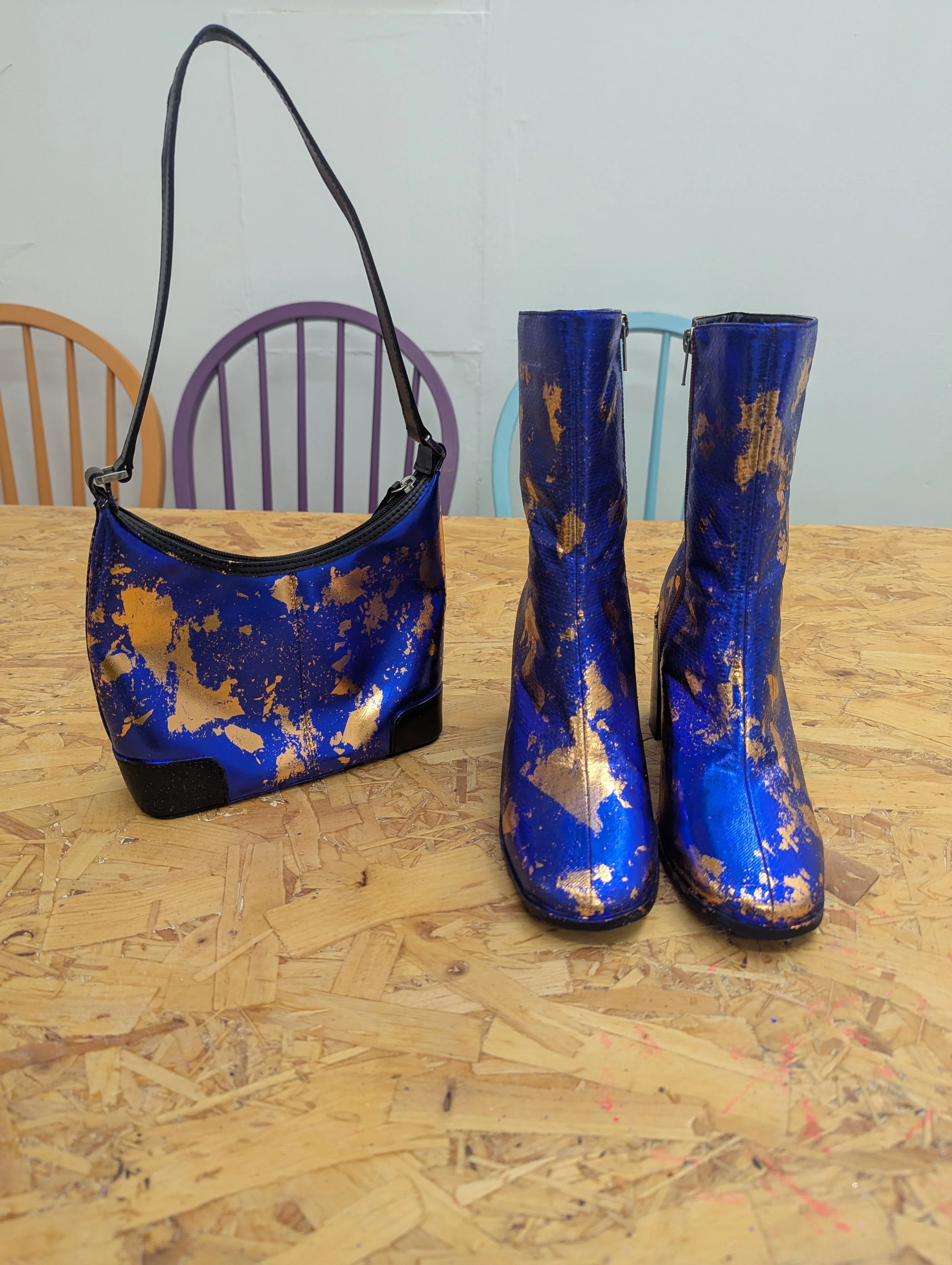 A matching set of blue and gold splatter-pattern purse and knee-high boots on a wooden table.