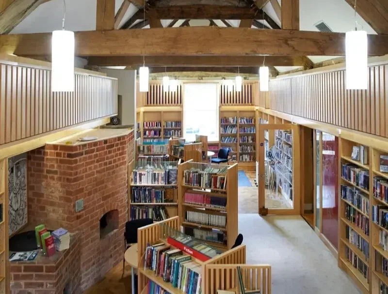 View of a two-story library with wooden shelves filled with books, a brick fireplace, and a cozy reading area illuminated by hanging pendant lights.