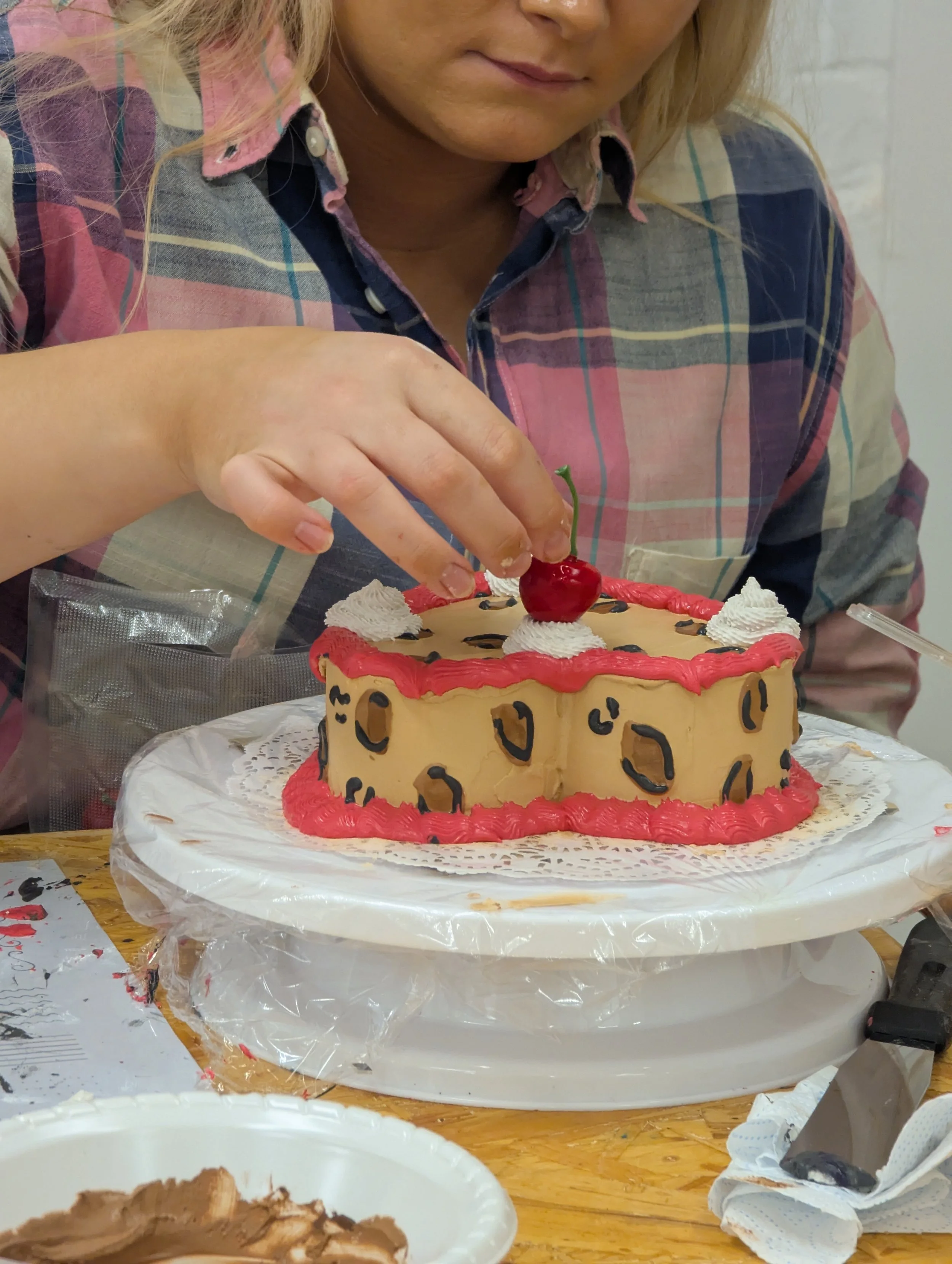Woman decorating a leopard print cake with a cherry on top.