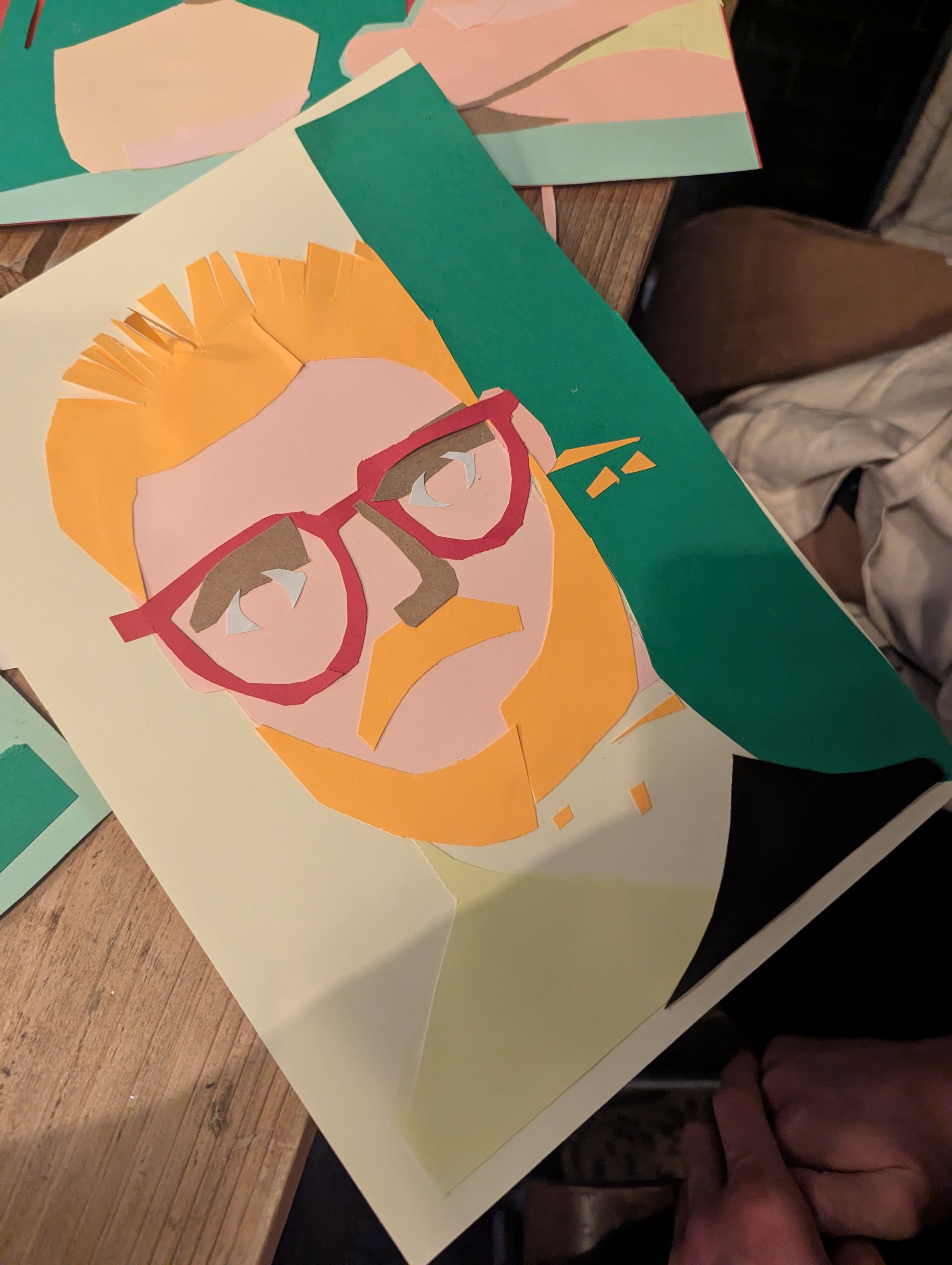 Colorful paper collage portrait of a man with orange hair, beard, and glasses on white background.