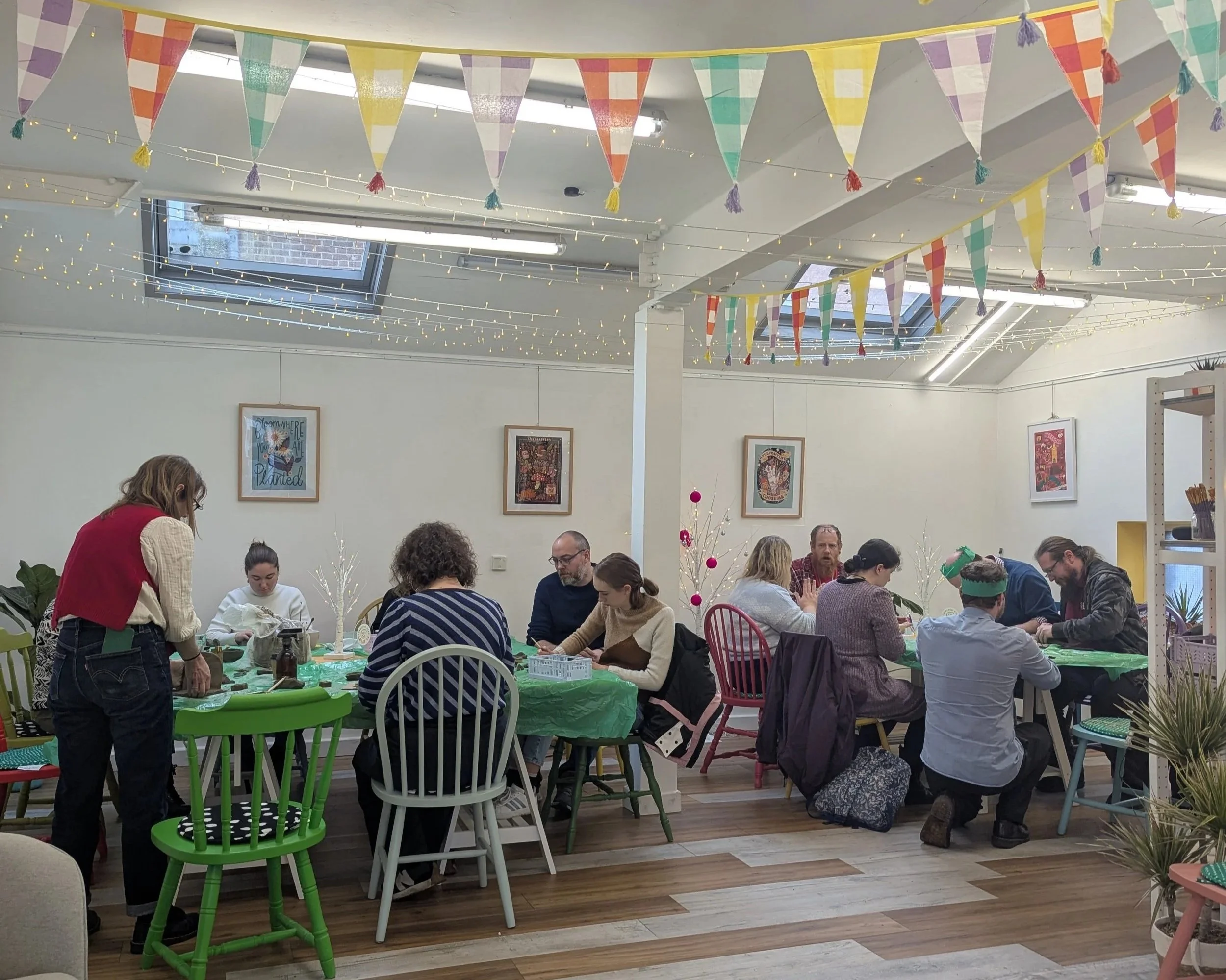 People gathered around tables in a decorated indoor space, celebrating a festive occasion with colorful pennant banners and string lights.