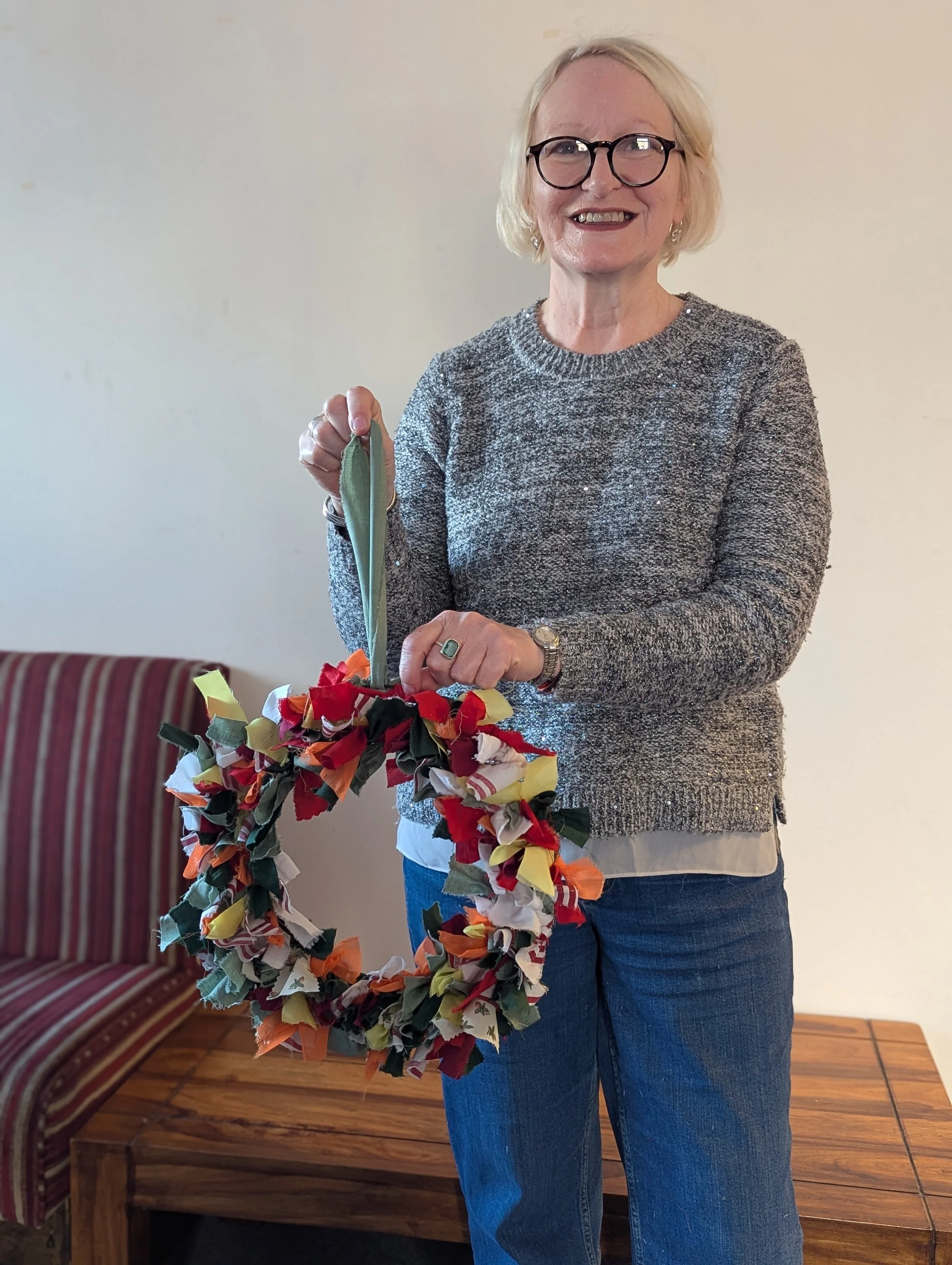 Woman with glasses smiling, holding a colorful fabric wreath