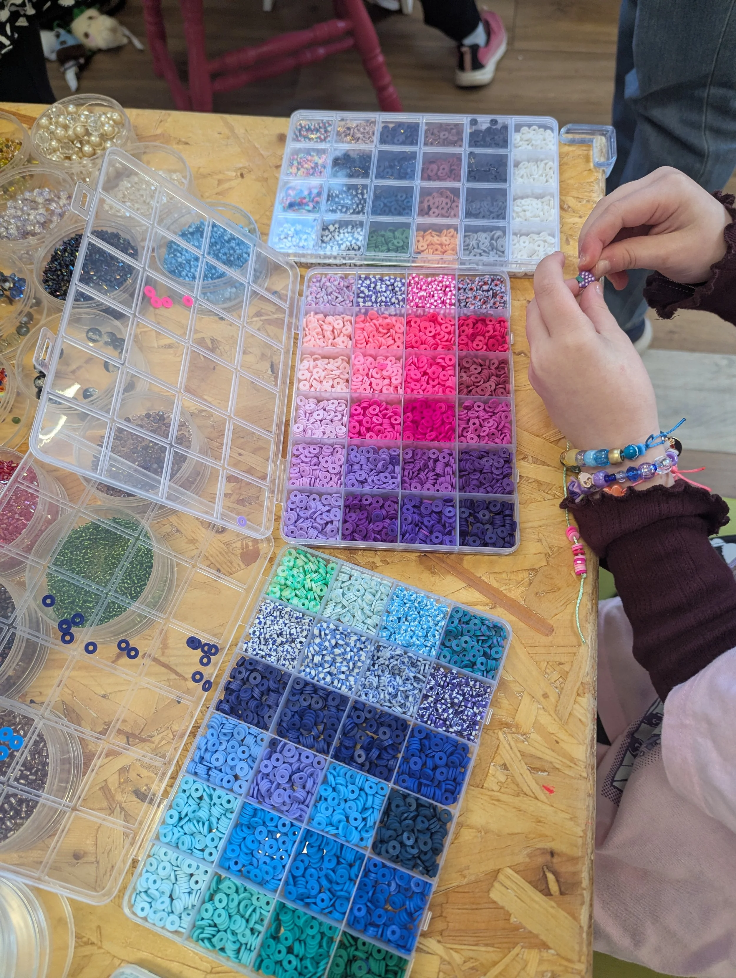 Person organizing colorful beads in small compartment boxes on a wooden table for jewelry making.