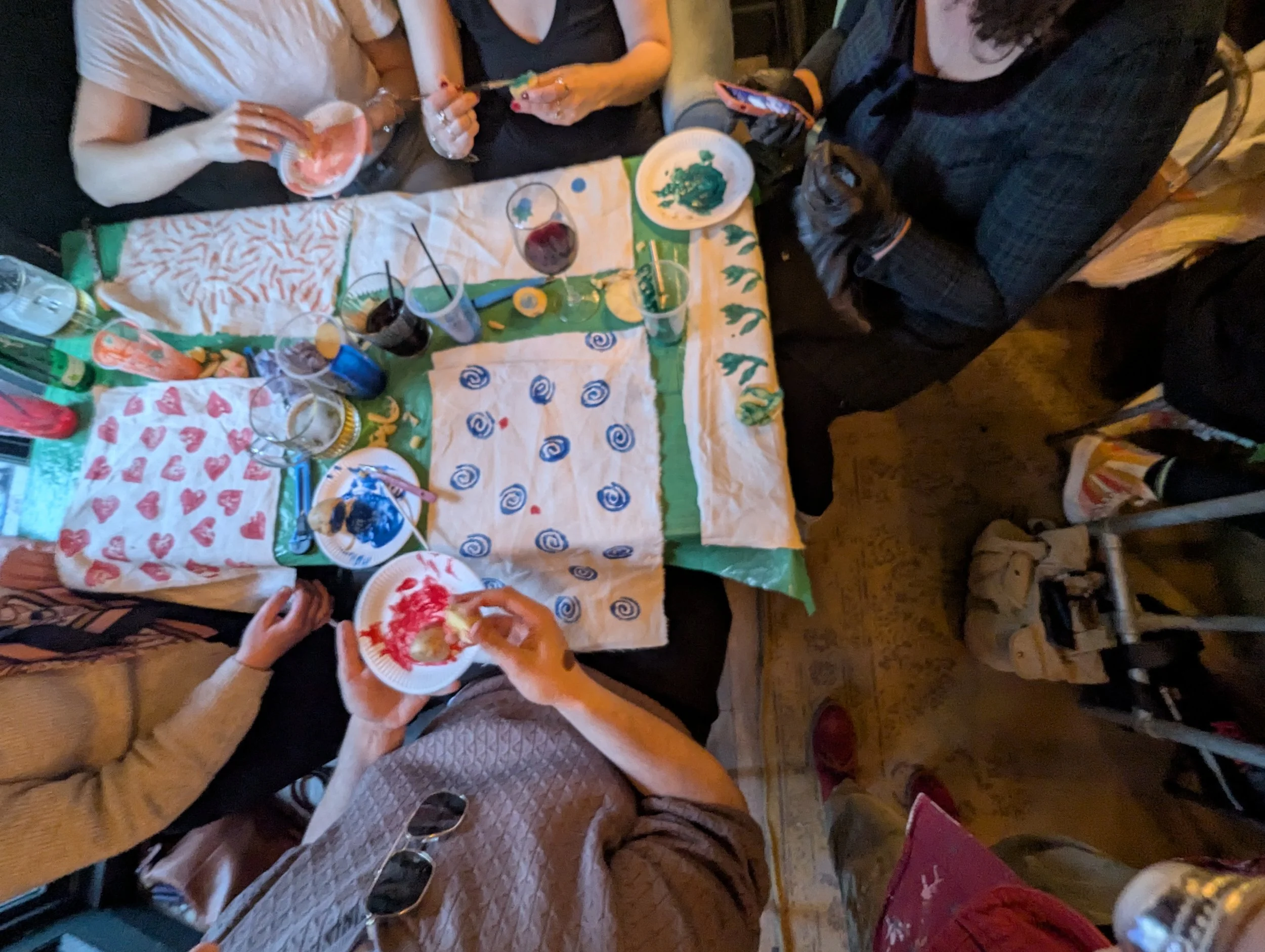 People seated around a table with colorful decorations, painting on paper plates, and drinks, celebrating with a craft activity.