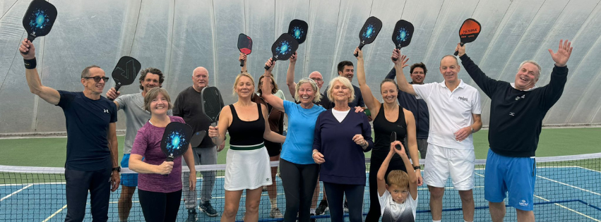 Group of people on an indoor tennis court celebrating, holding paddles with the galaxy design, and some raising their hands.