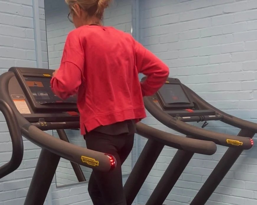 A woman on a treadmill in a gym, wearing a red jacket and black pants.