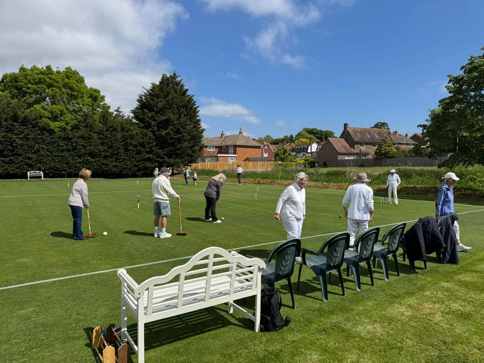 People playing lawn bowls on a green field on a sunny day, with houses and trees in the background.