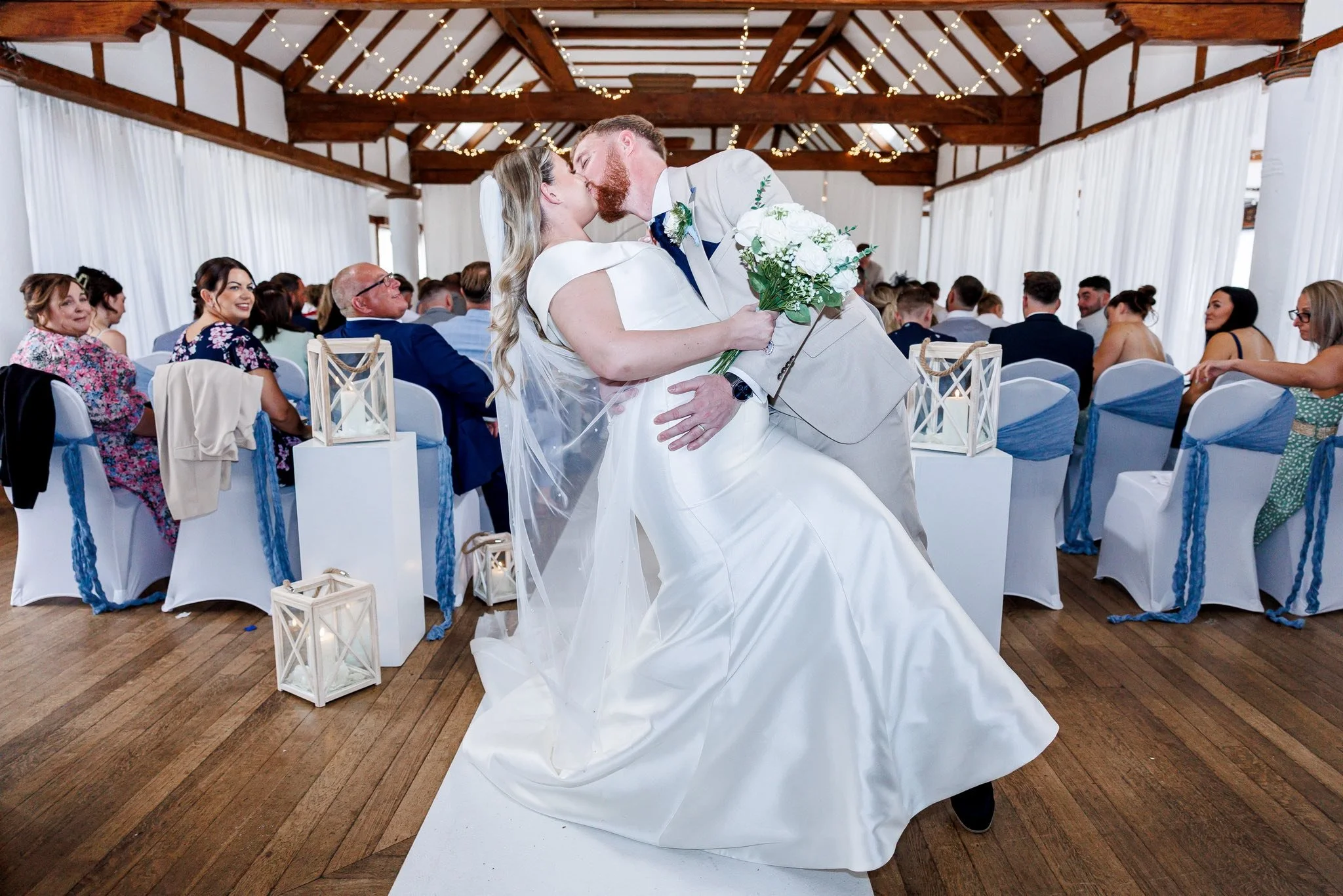 A bride and groom sharing a kiss during their wedding ceremony, with guests seated in the background.