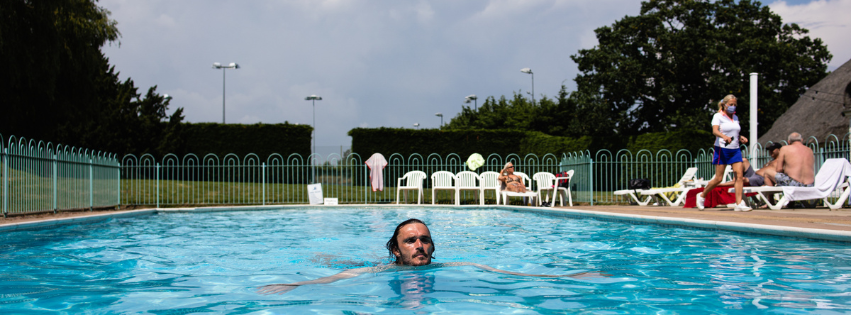 A man swimming in an outdoor pool with lounge chairs and people relaxing around the pool area.